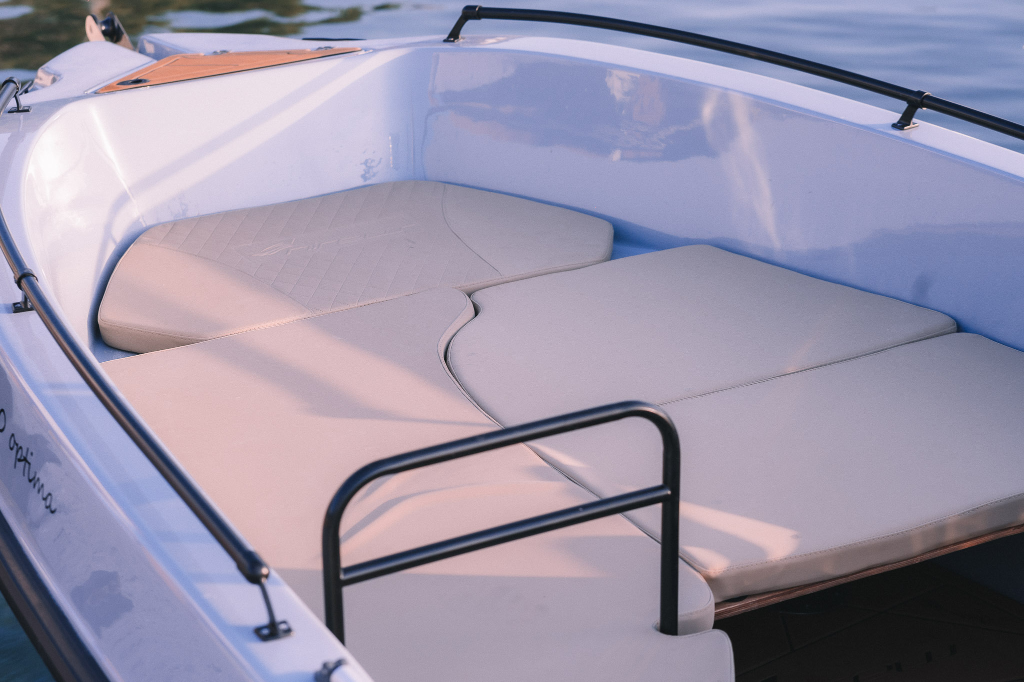 White motor yacht bow seating area with beige cushions and safety railings on calm water