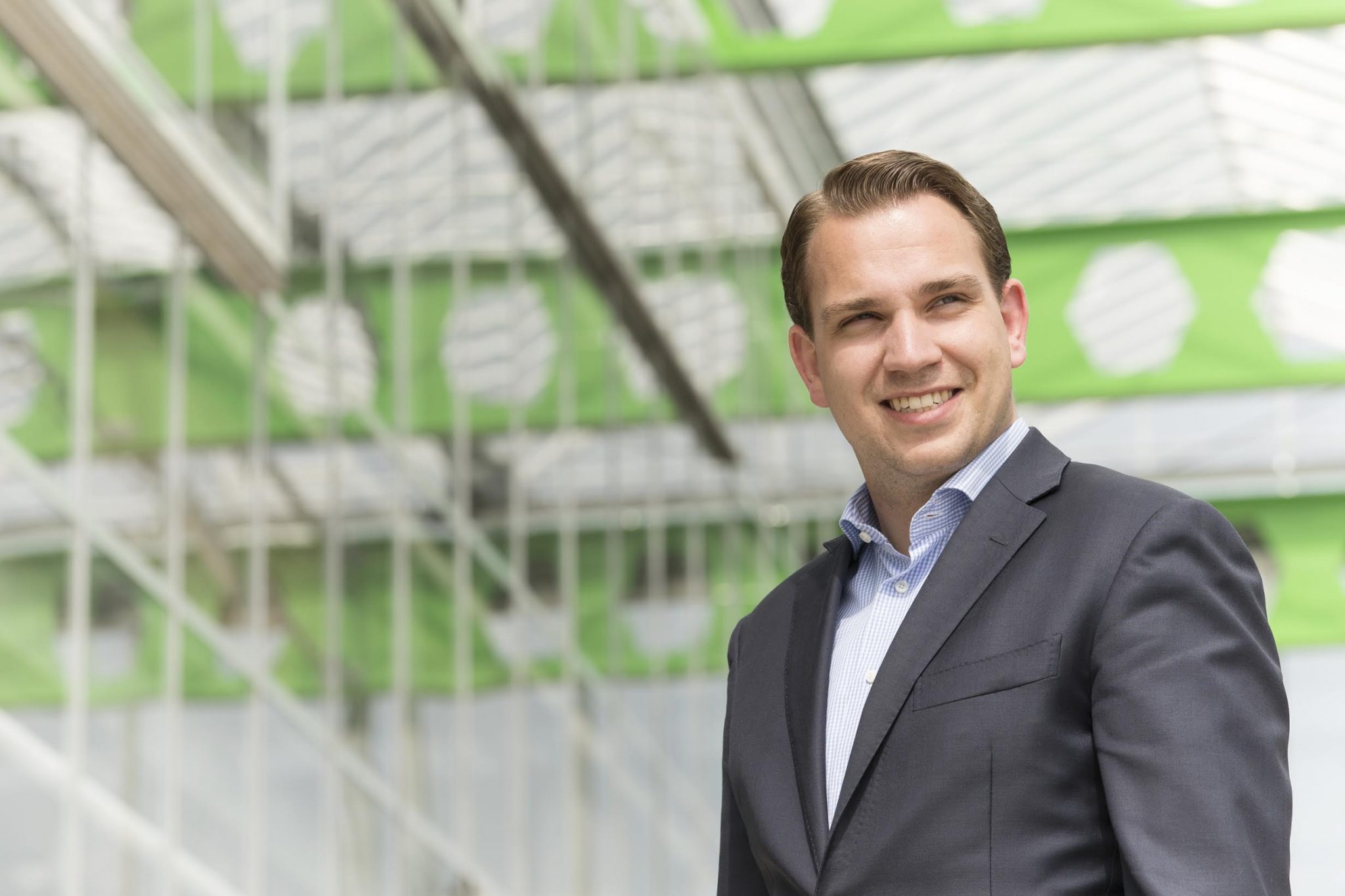 Smiling young woman with curly hair sitting at a laptop, in front of a teal wall.