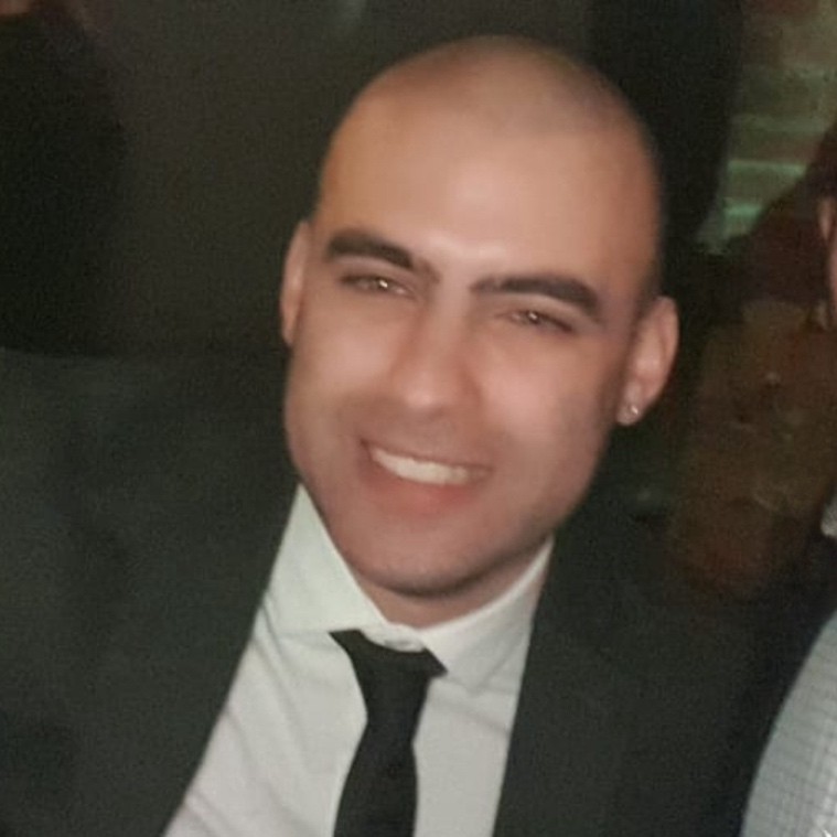 Close‑up photo of a person in formal attire against a dark background.