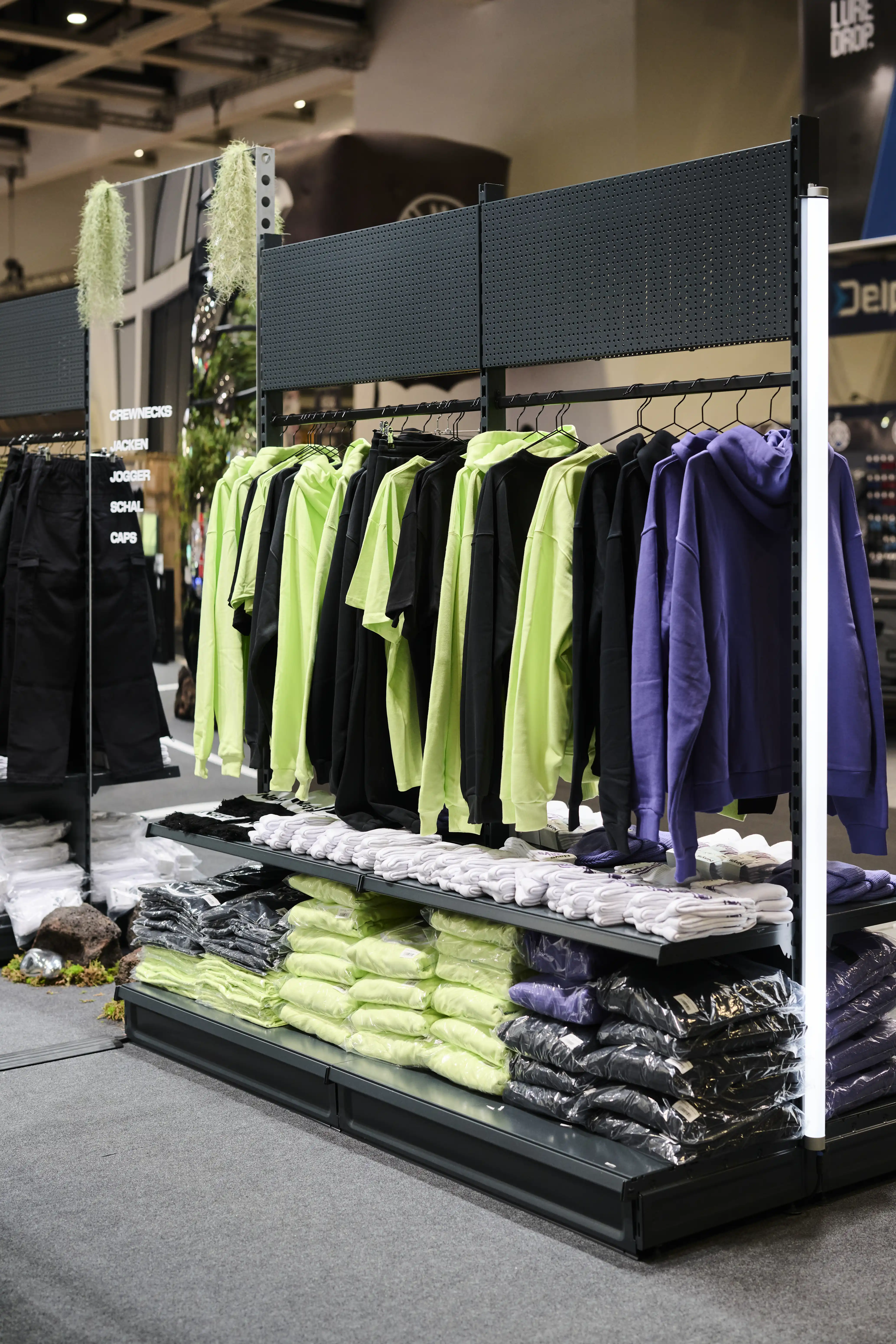 Apparel rack with black, neon-green and purple Nays hoodies and folded shirts at the trade fair booth.