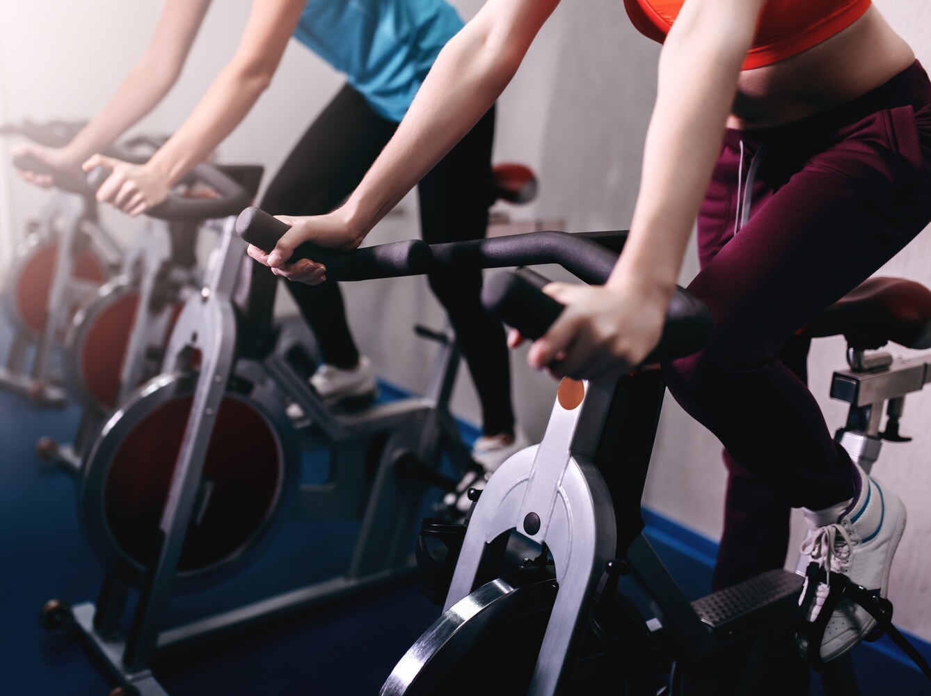 two women learning how to lose weight on exercise bike by using stationary bikes at the gym