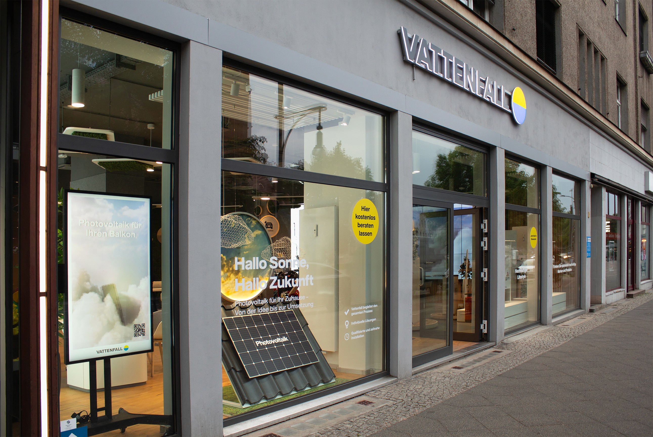 Street view of the Vattenfall store in Pankow, Berlin, featuring large glass windows displaying services for solar energy, heat pumps, and e-mobility, promoting sustainable home energy solutions