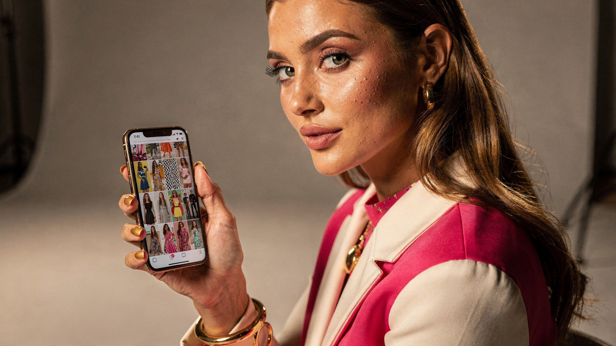 Lifestyle creator looking at a phone showing a profile grid of vertical thumbnails