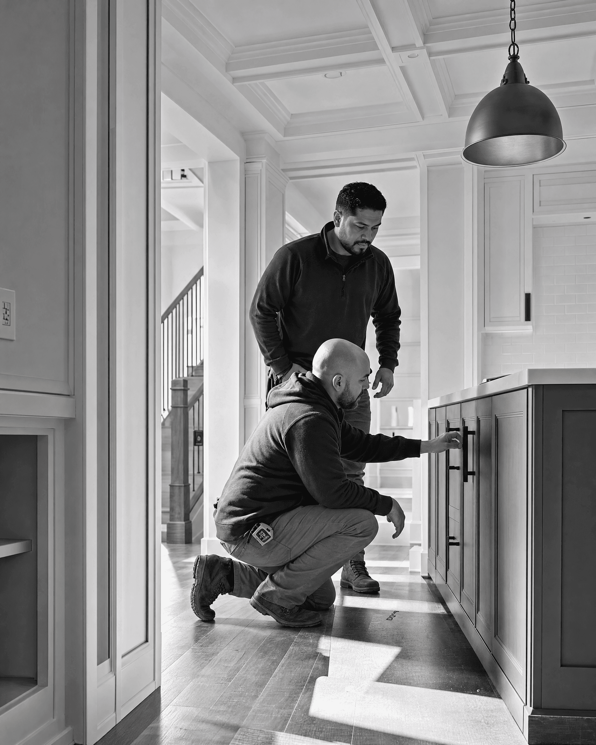 Two construction professionals reviewing cabinet hardware and finish details in a near-complete kitchen renovation.