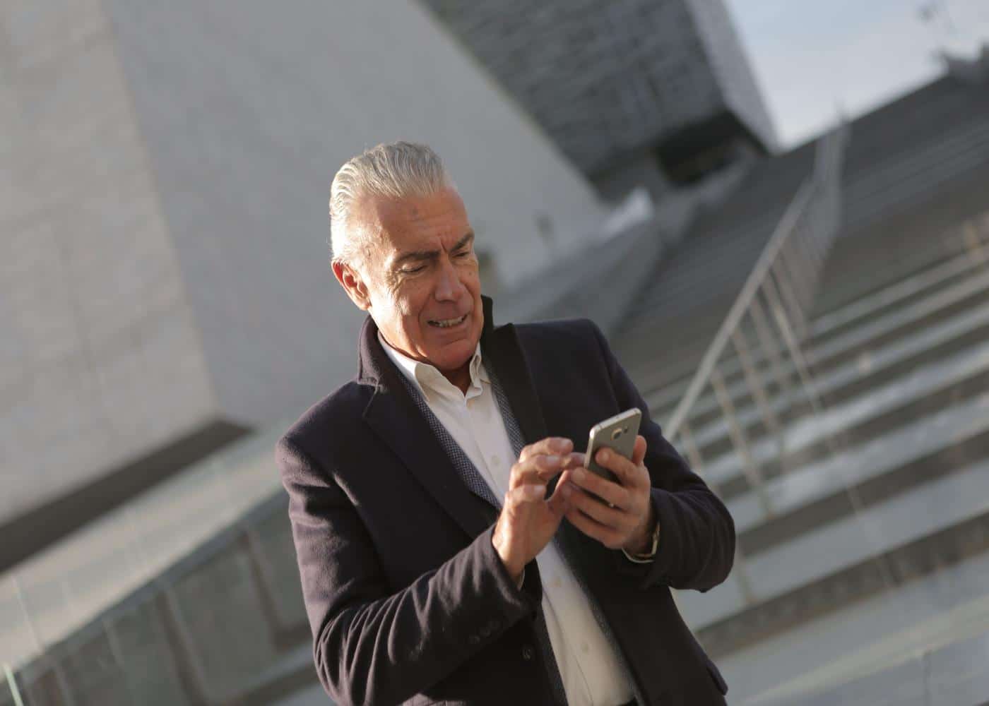 Man outside with black blazer looking at smartphone