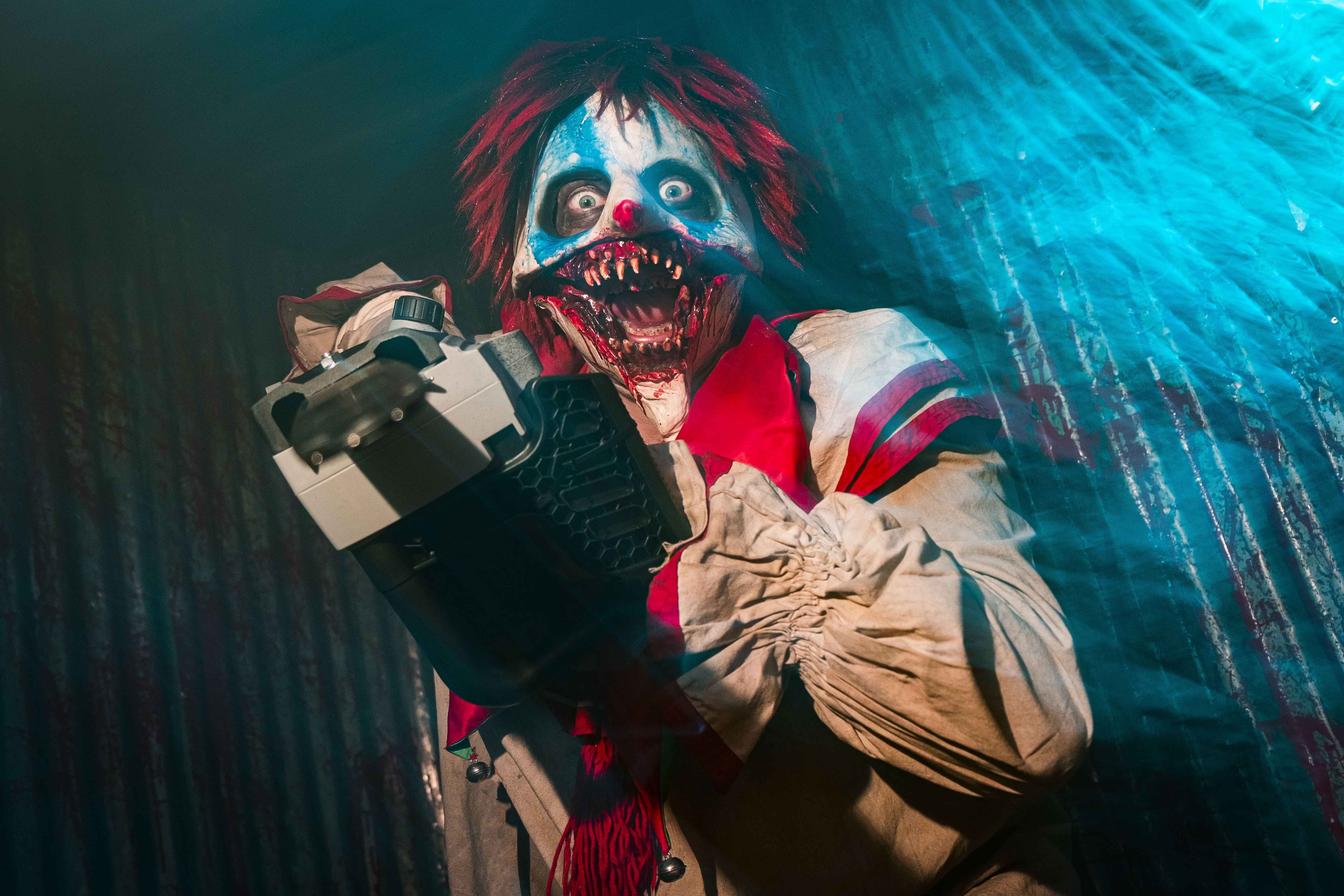 A terrifying clown character with wild red hair and exaggerated makeup brandishes a chainsaw under eerie blue lighting, creating a spooky atmosphere ideal for Halloween-themed content and horror film promotions.