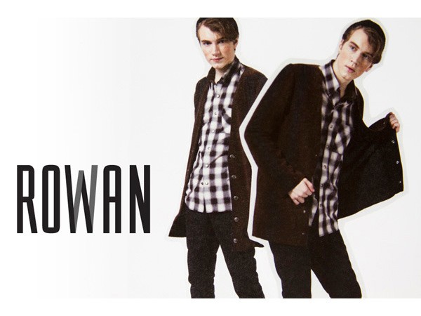 Two young men stand side by side against a white background. The man on the left wears a black and white checkered shirt under a dark cardigan and dark pants. The man on the right wears a dark jacket over a similar checkered shirt and dark pants. Both have short brown hair. The word "ROWAN" is displayed in bold black letters to the left of the men.