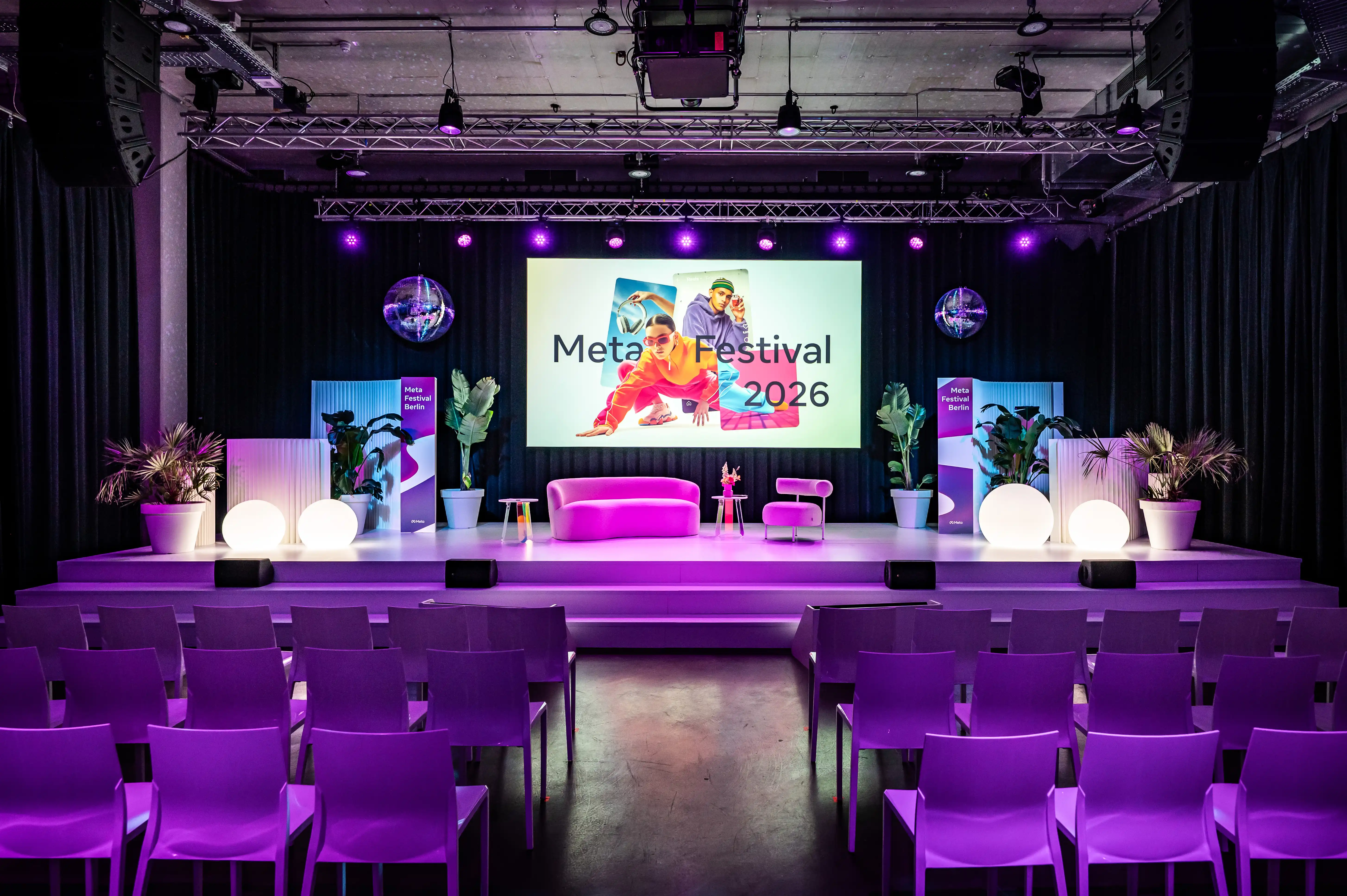 Meta Festival 2026 stage with pink sofa, plants, glowing spheres and purple chairs in front.