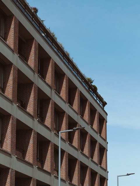 Modern bakstenen appartementengebouw met een groene daktuin tegen een blauwe lucht
