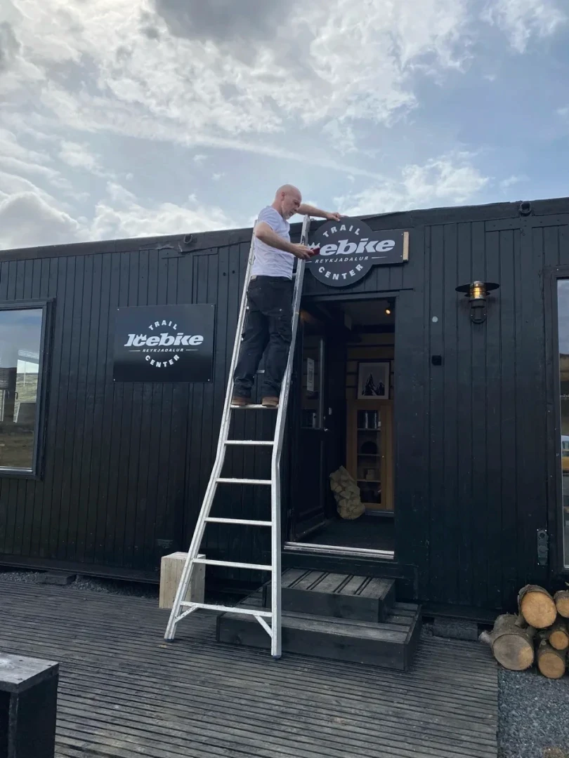 Man in a ladder putting a sign up at reykjadalur trailcenter