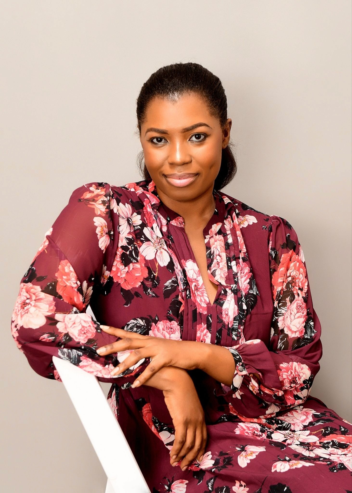 Abigail Owusu seated in floral dress, posing confidently in studio for Hairylin Organics founder feature.