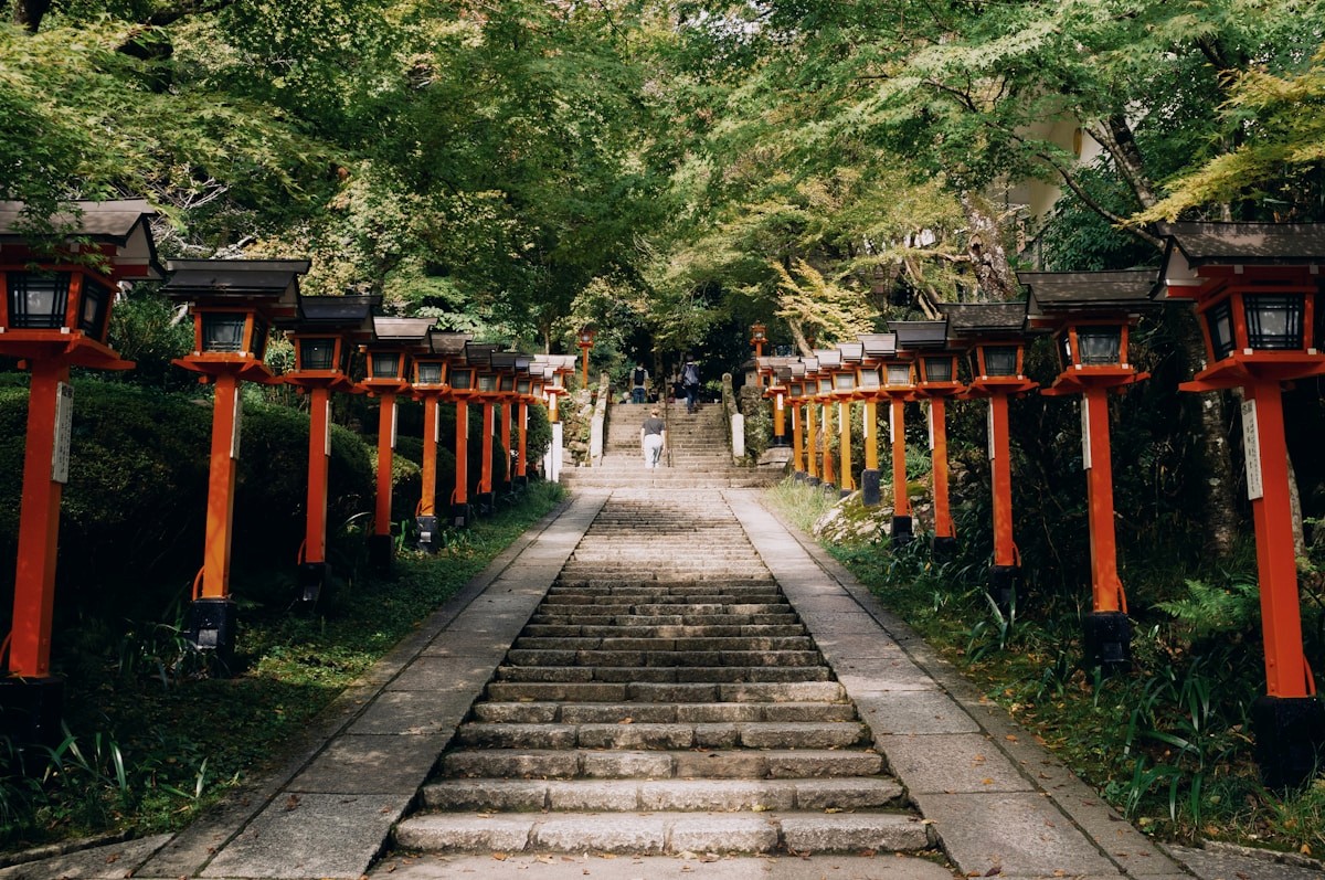 Red lantern-lined stone stairs leading through a temple forest in Kyoto