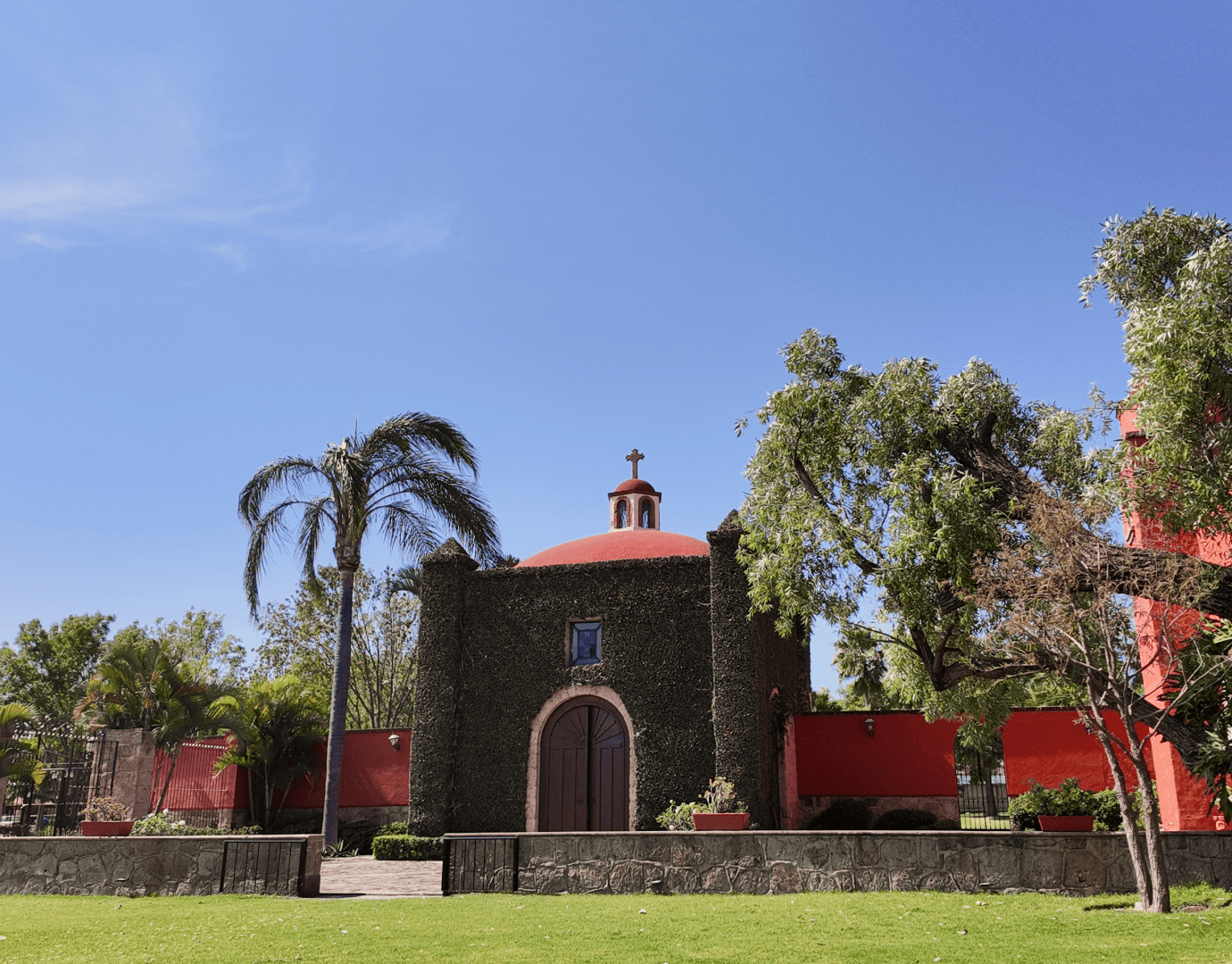 An elegant wedding ceremony setup features a domed gazebo adorned with peach and pink floral arrangements and lush greenery. White chairs line the aisle.