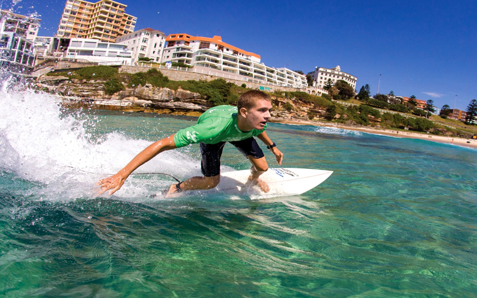 Surfer che cavalca un'onda a Bondi Beach con edifici costieri sullo sfondo.