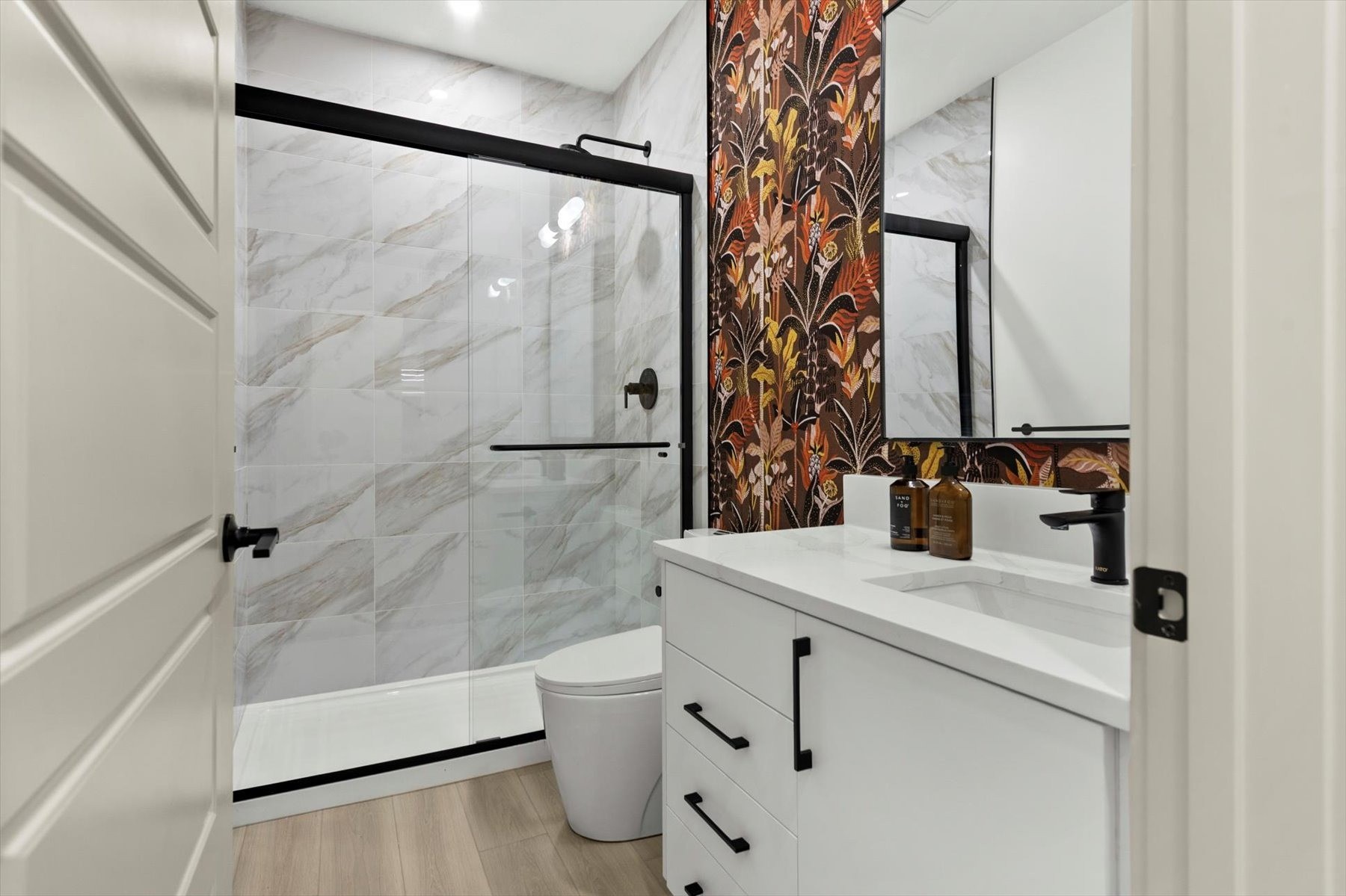 Legal suite bathroom after: marble-look shower with black glass door, botanical wallpaper and a white vanity