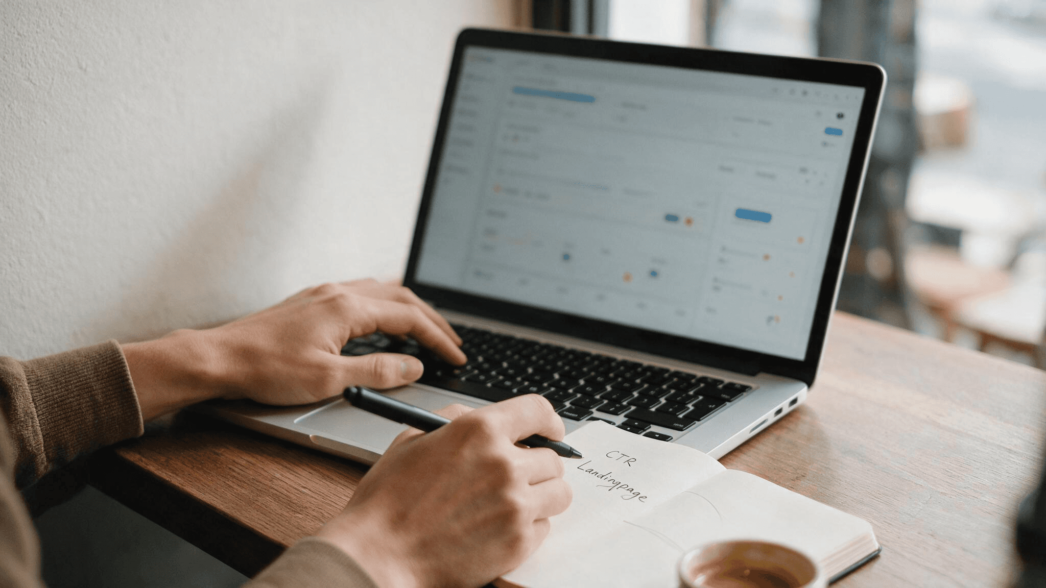 Nahaufnahme eines Marketers beim Optimieren von Google Ads Kampagnen am Laptop mit Notizblock