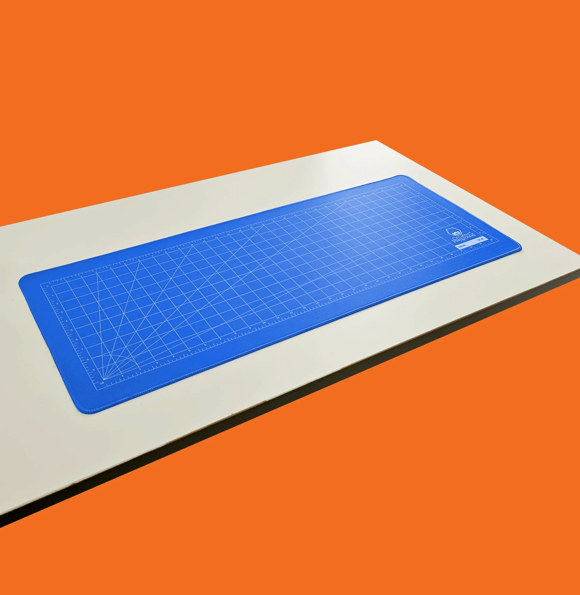 Blue cutting mat deskmat on a white desk against an orange background