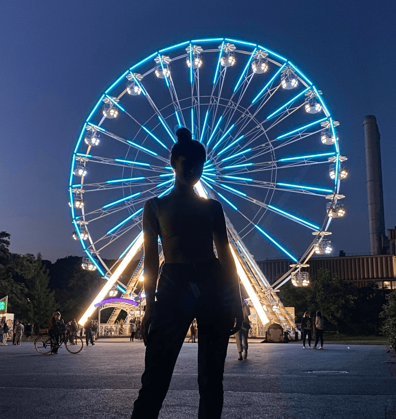 Silhouette of a woman standing in front of a colorful ferris wheel