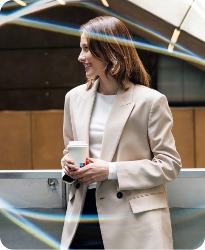 A smiling professional woman in a beige blazer holding a coffee cup, representing efficient time management for business and corporate productivity in a modern office environment.