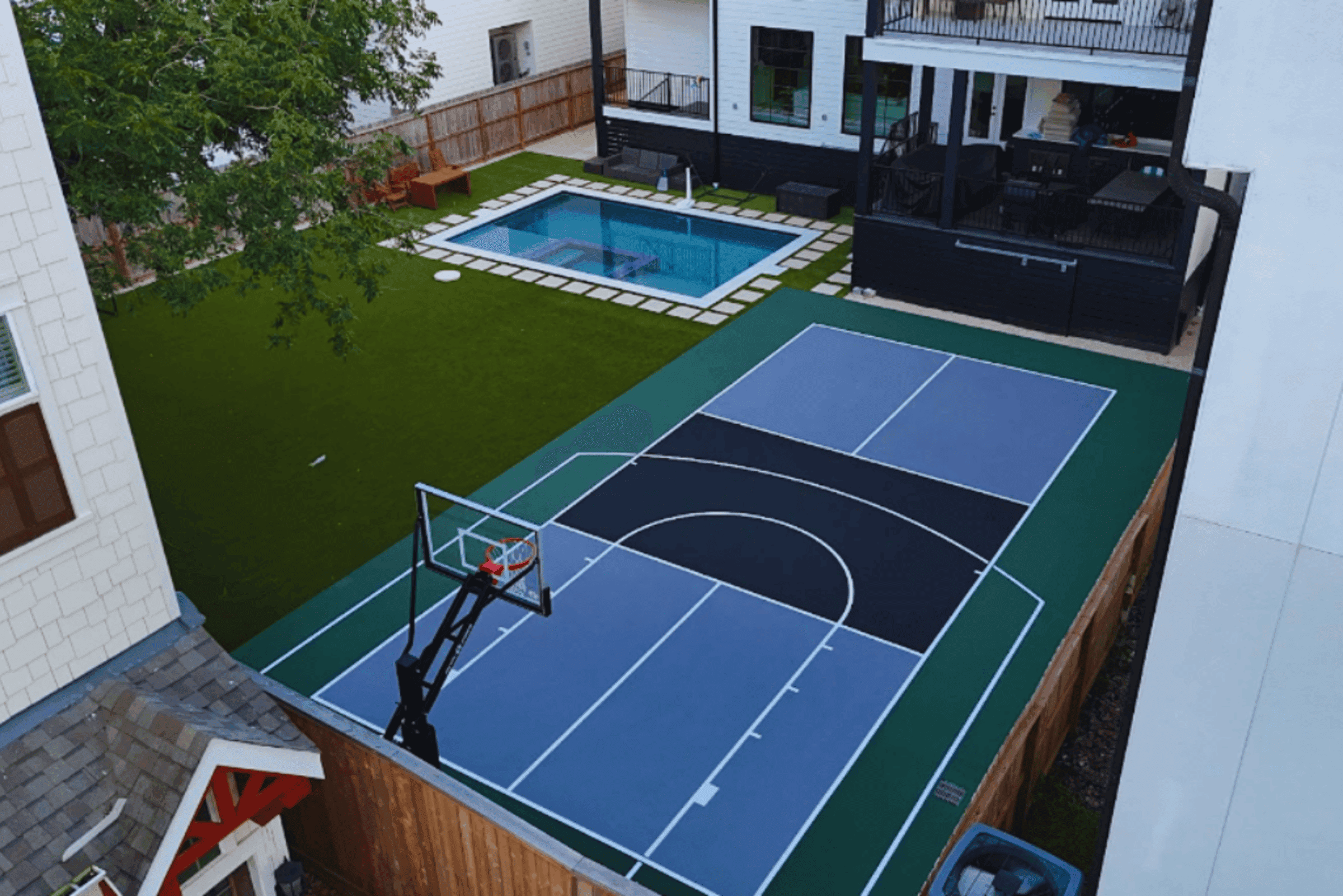 Professional navy blue and green multi-sport court by BuildMyCourts Texas pickleball court builders featuring basketball hoop and modern residential backyard design with pool
