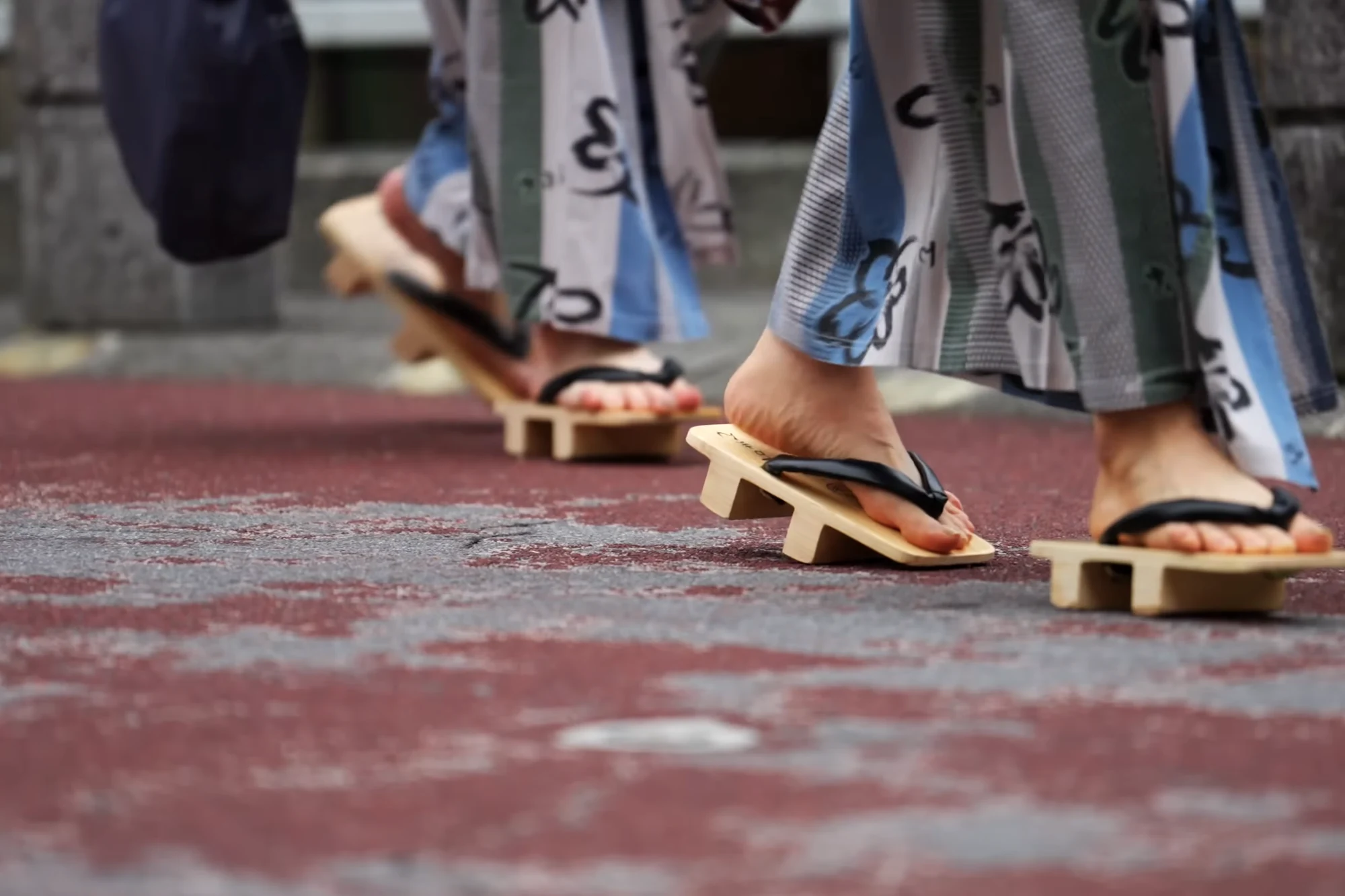 Close view of feet in wooden geta and yukata hems mid-stride on a Kinosaki street.