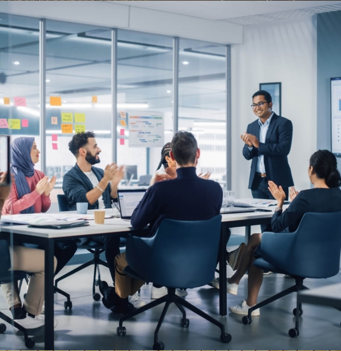 A business meeting in a conference room, with a speaker addressing a group seated at a table.