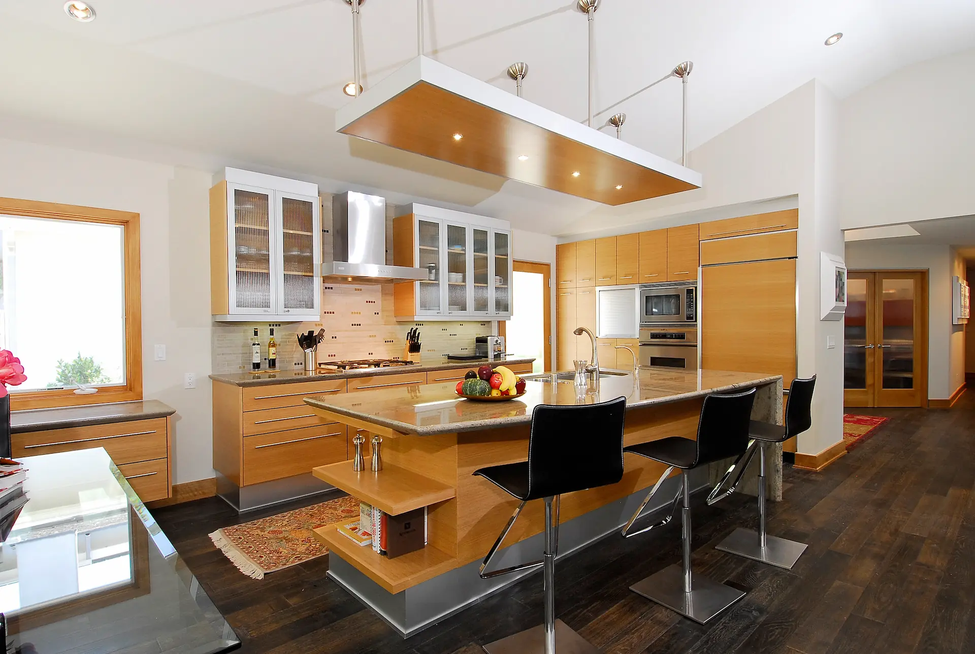 Modern kitchen with wooden cabinets, central island, hanging lights, and dark flooring. Irvine Transitional Modern. Photo by Chris Darnall.