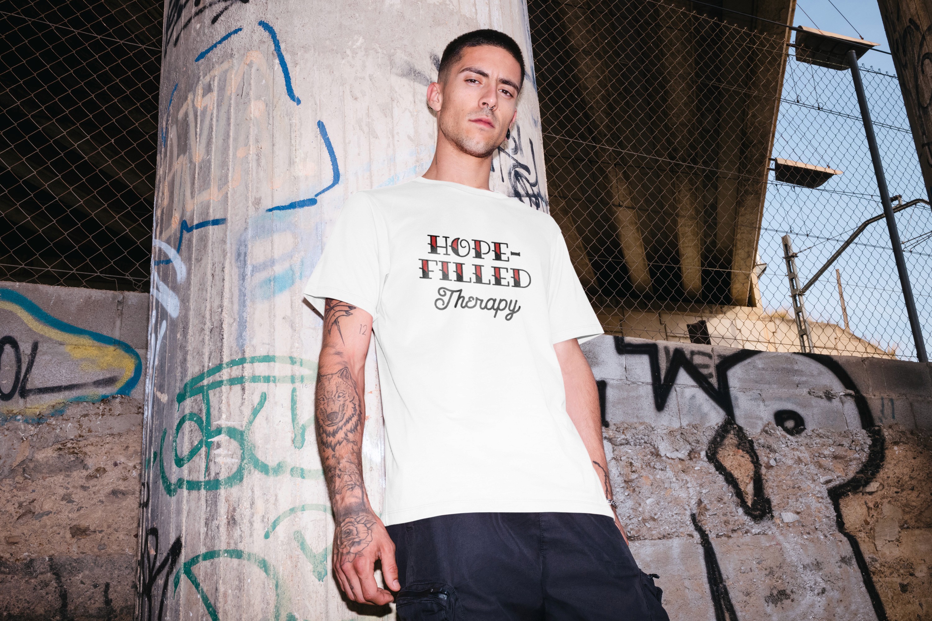 Model wearing a white Hope-Filled Therapy branded t-shirt against a graffiti-covered urban backdrop.
