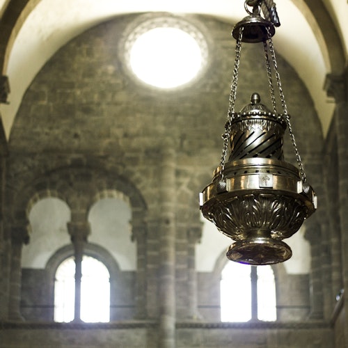 Un grande turibolo metallico ornato pende da catene in una cattedrale con finestre ad arco e mura di pietra.