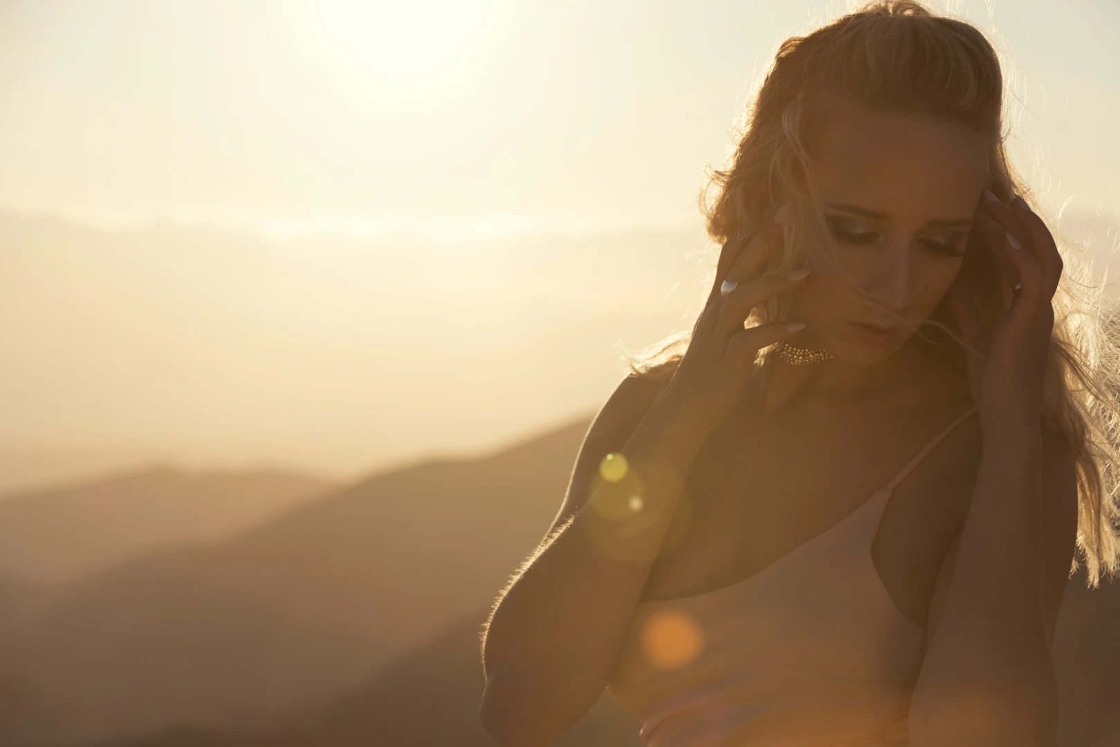 The artist, illuminated by the setting sun, adjusting her hair with a mountainous backdrop.