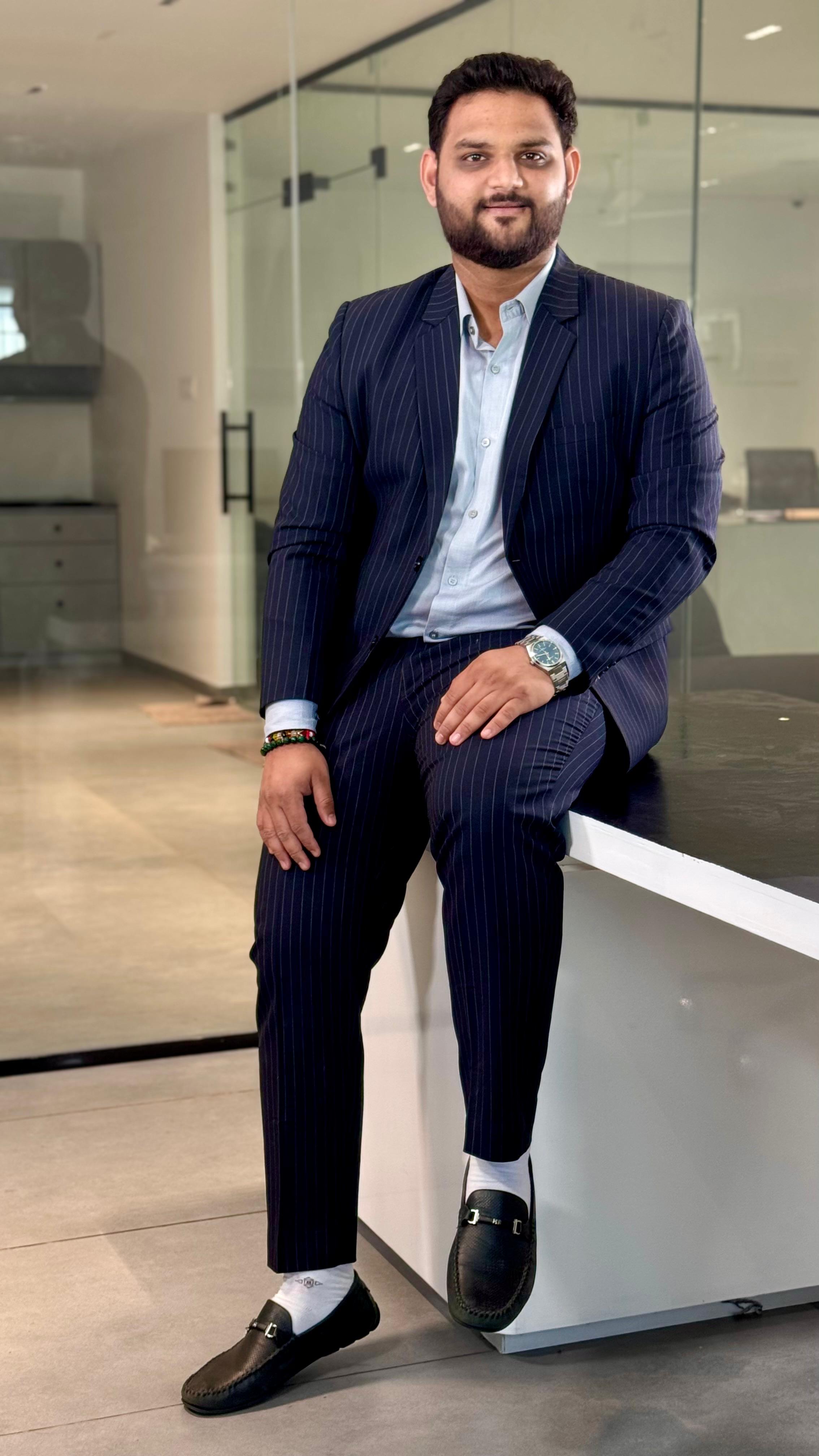 A person with medium-length brown hair wearing a dark, textured coat and a burgundy turtleneck. They have a calm, neutral expression.