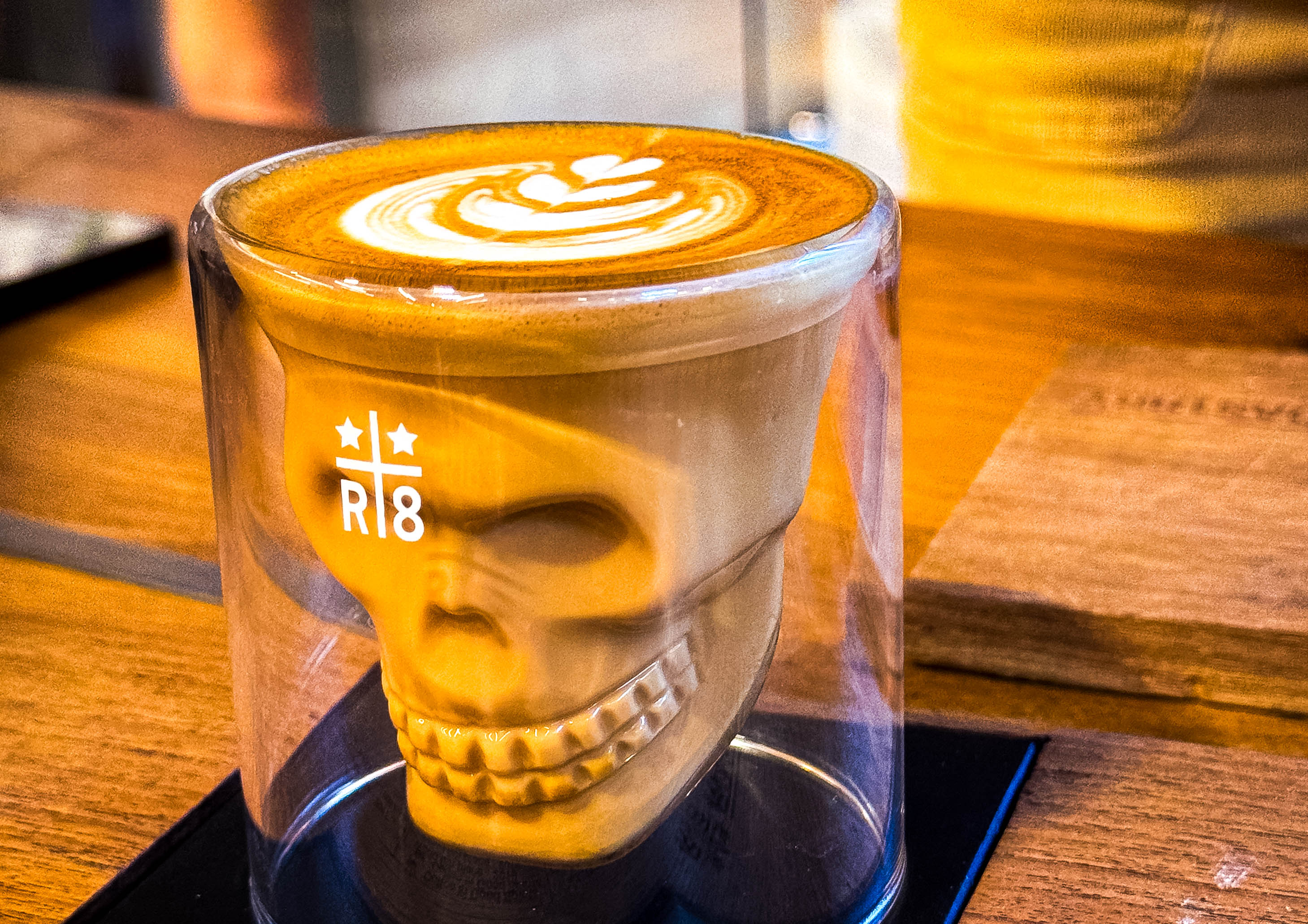 a machhiato espresso drink in a clear cup that is in the shape of a skull with latte art on top