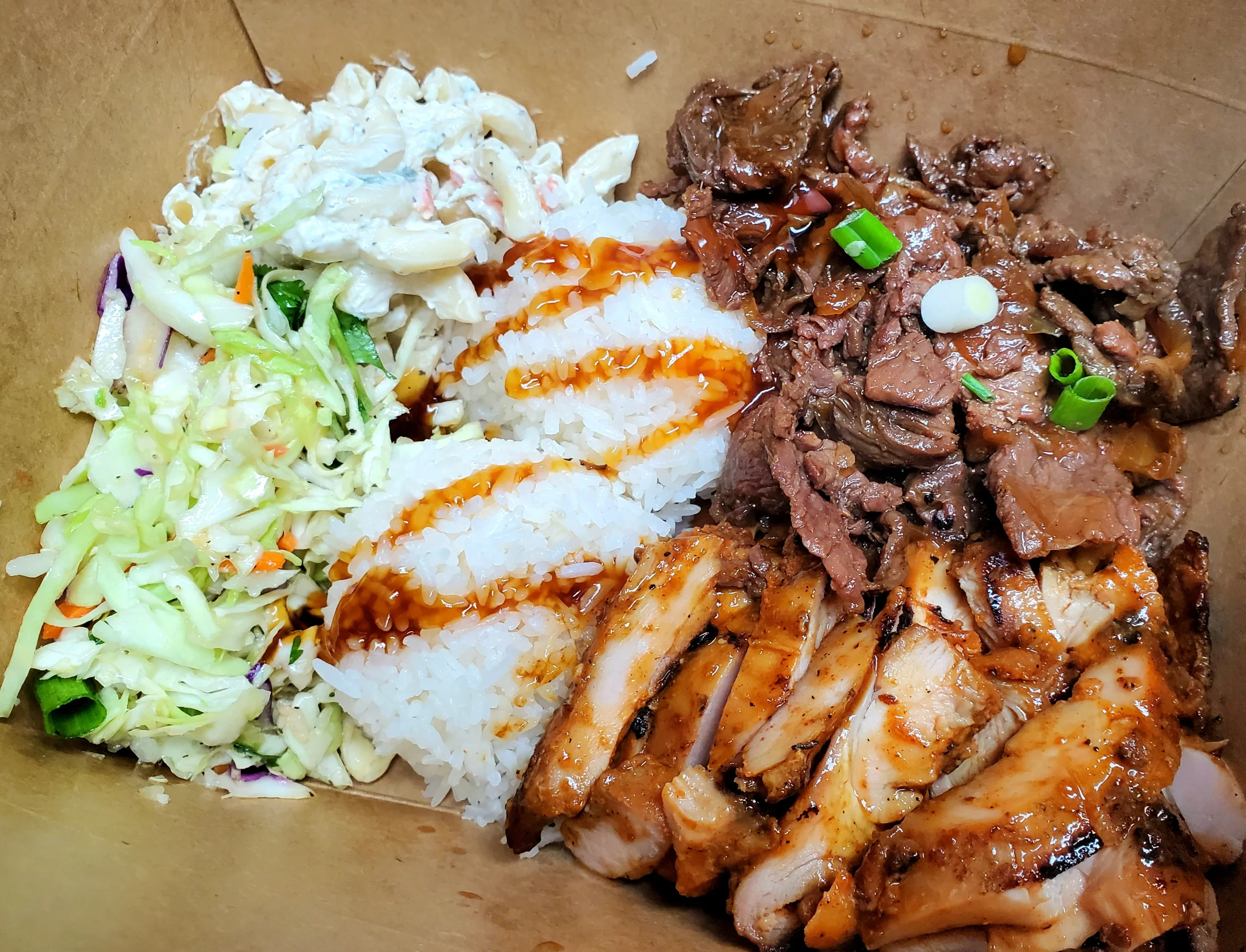 A hearty Hawaiian BBQ combo plate featuring char-grilled Huli Huli chicken, savory Hawaiian beef, two scoops of Jasmine rice, creamy mac salad, and fresh Asian slaw in a takeout container.