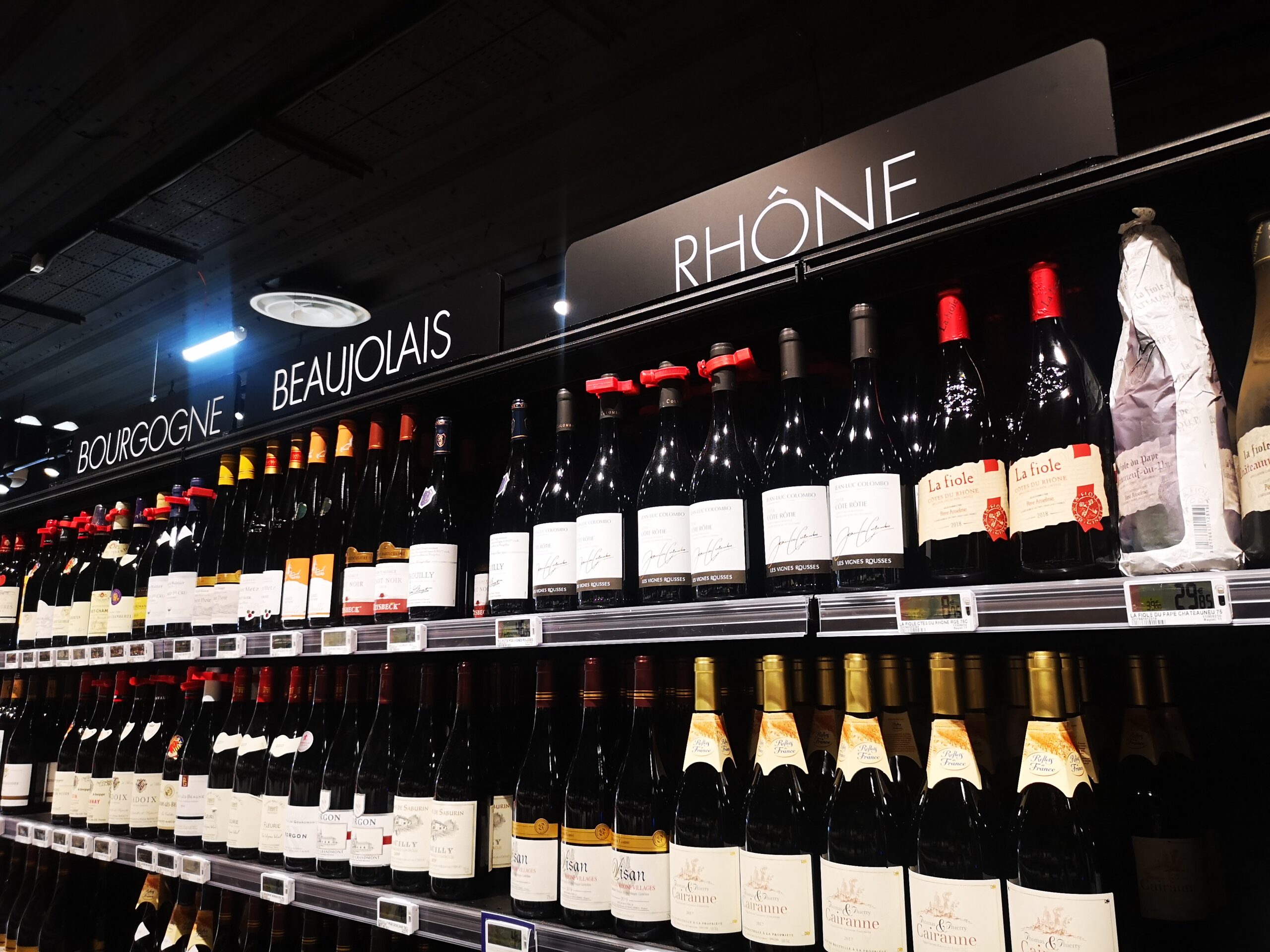 Étagère de magasin présentant des rangées de bouteilles de vin rouge provenant des régions de Bourgogne, du Beaujolais et du Rhône, avec des étiquettes élégantes sous un éclairage tamisé.