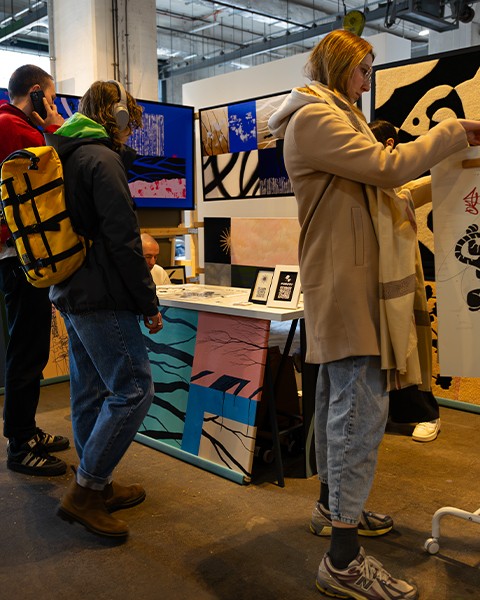 Zdjęcie przedstawiające kilka osób na targach, którzy oglądają obrazy i sztukę.