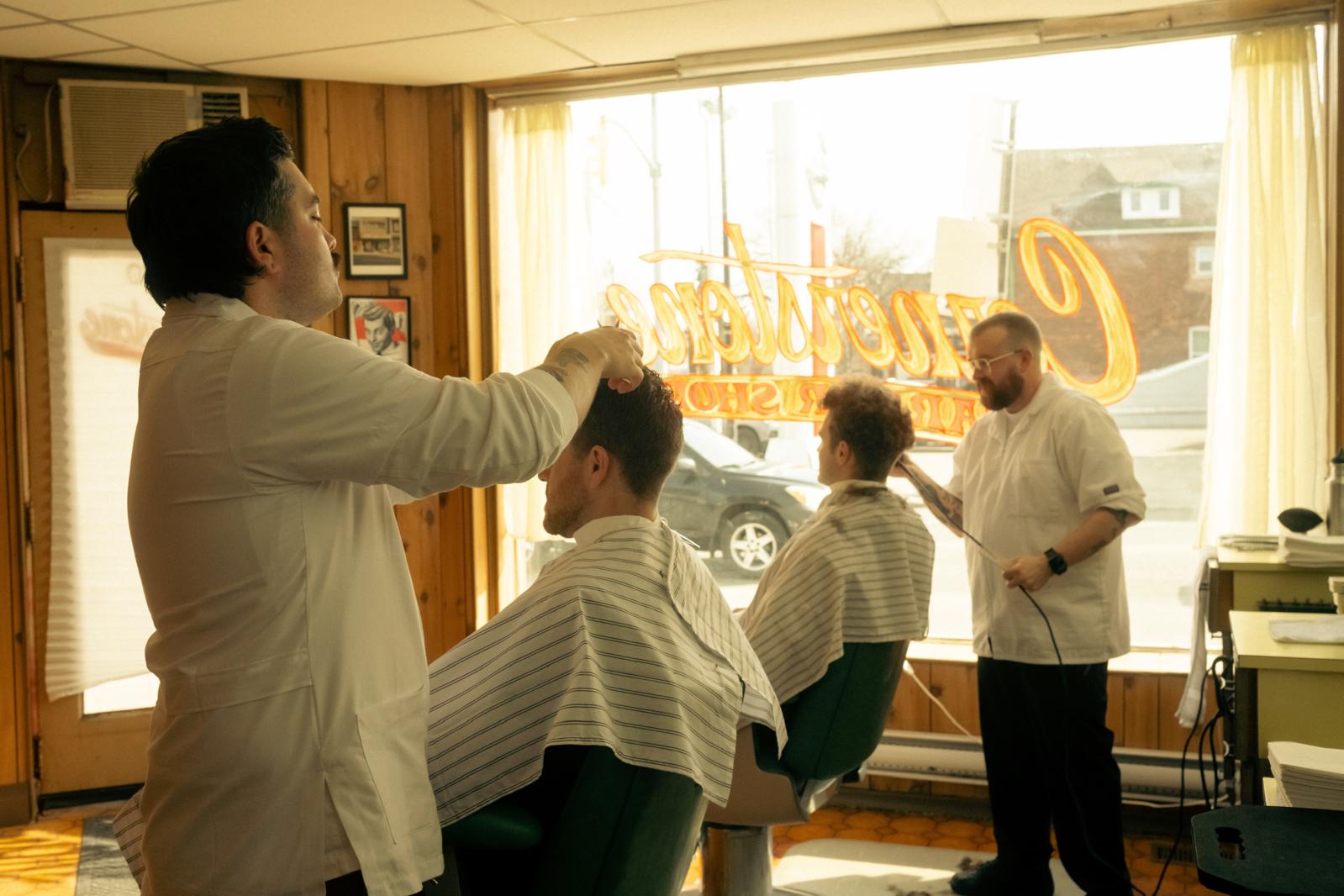 Two patrons getting their haircut, street-facing window in the background