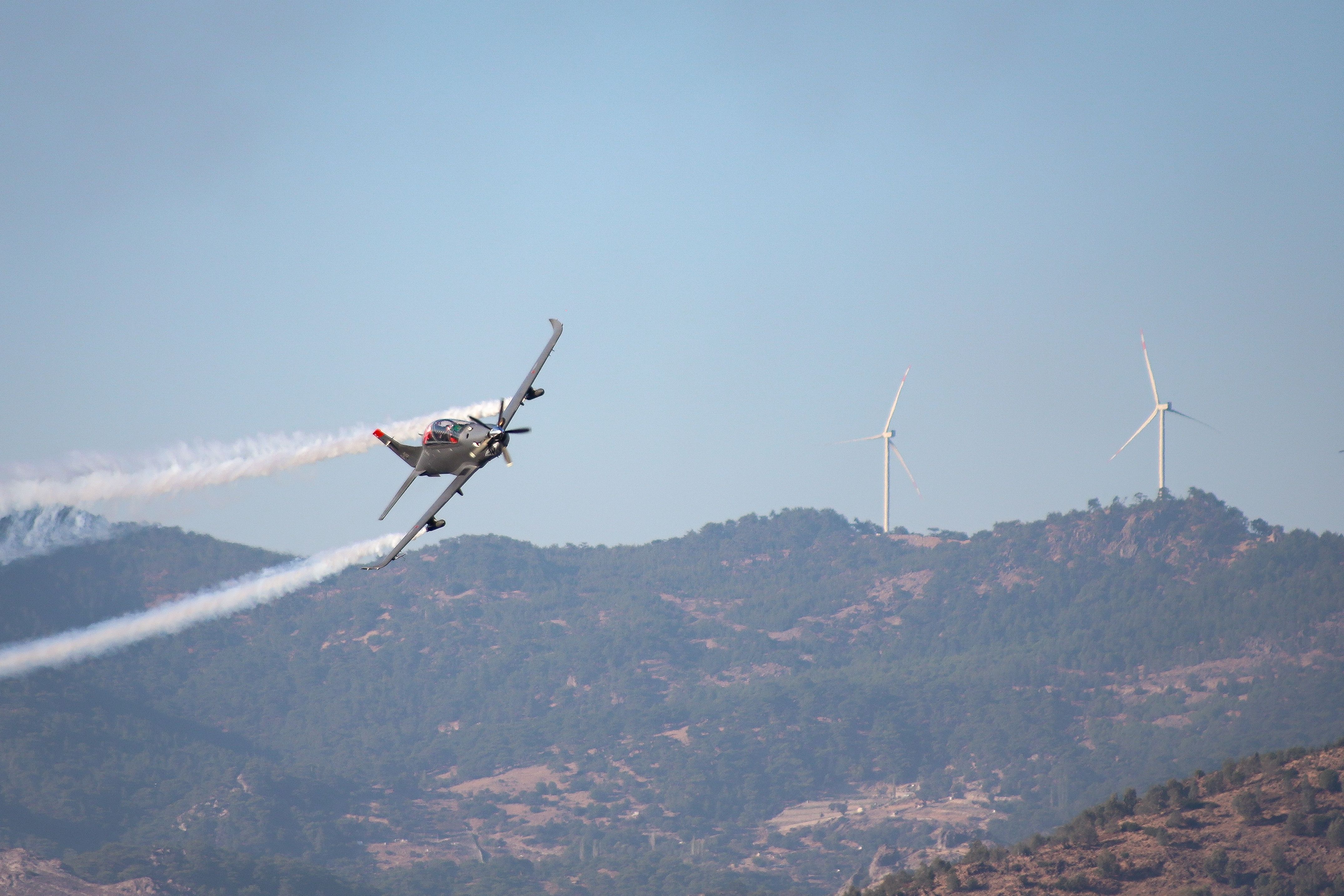 aerobatic-plane-with-smoke-trail-flying-over-the-mountains-with-wind-turbines-in - mehmet-ali-özuğur (pexels)