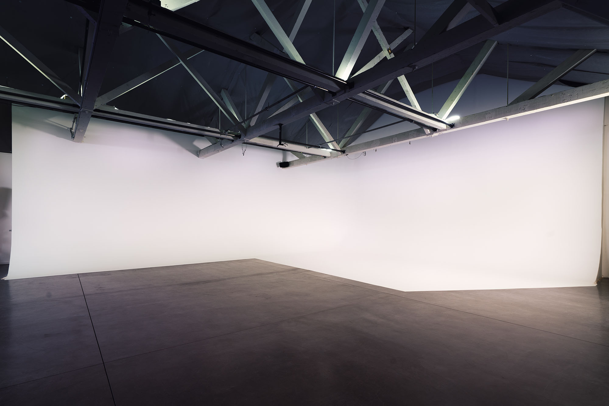 A wide image of the Cyc wall on the soundstage at Particle Studio in Seattle. The cyc wall is displayed in a 3/4 angle with white light splashing on the wall. 