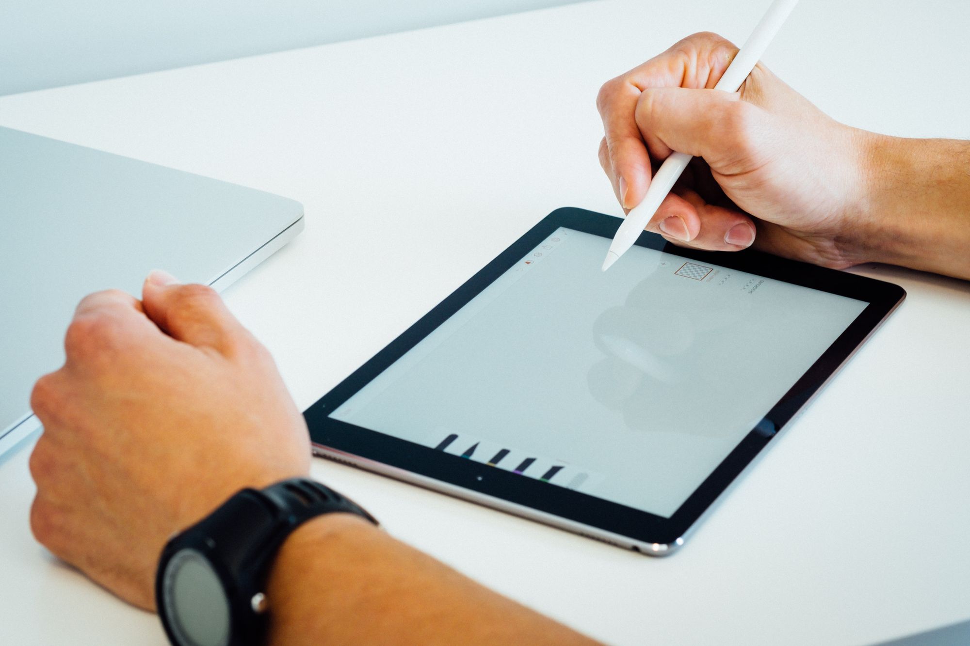 hands on a white table holding a stylus and a tablet in between them