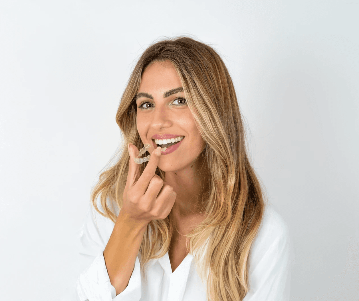 A woman smiles and holds invisalign clear aligners with a case, showcasing a certified invisalign provider at Bella Medical Centre