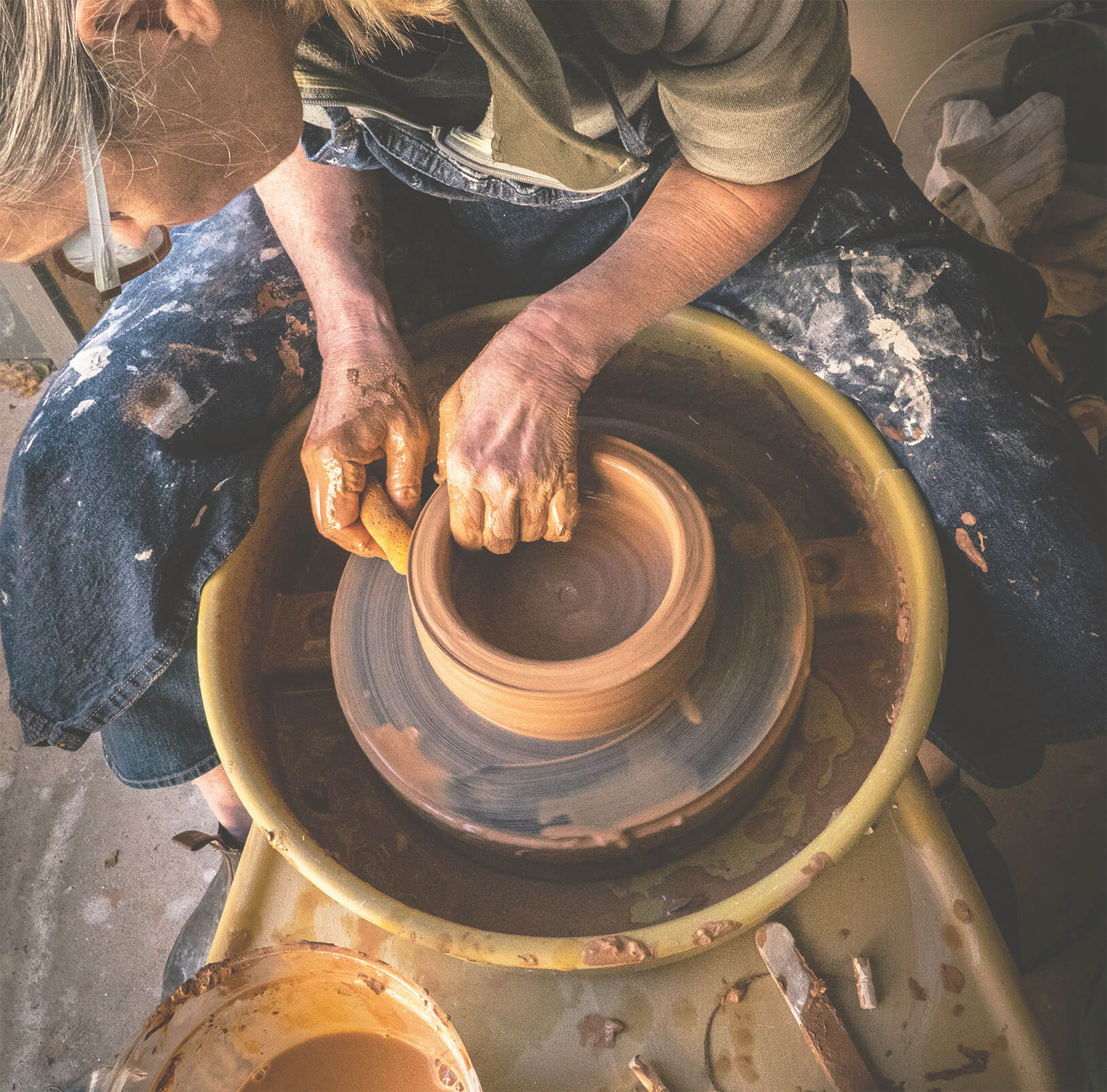 Hands shaping clay on a pottery wheel, creating a ceramic bowl.