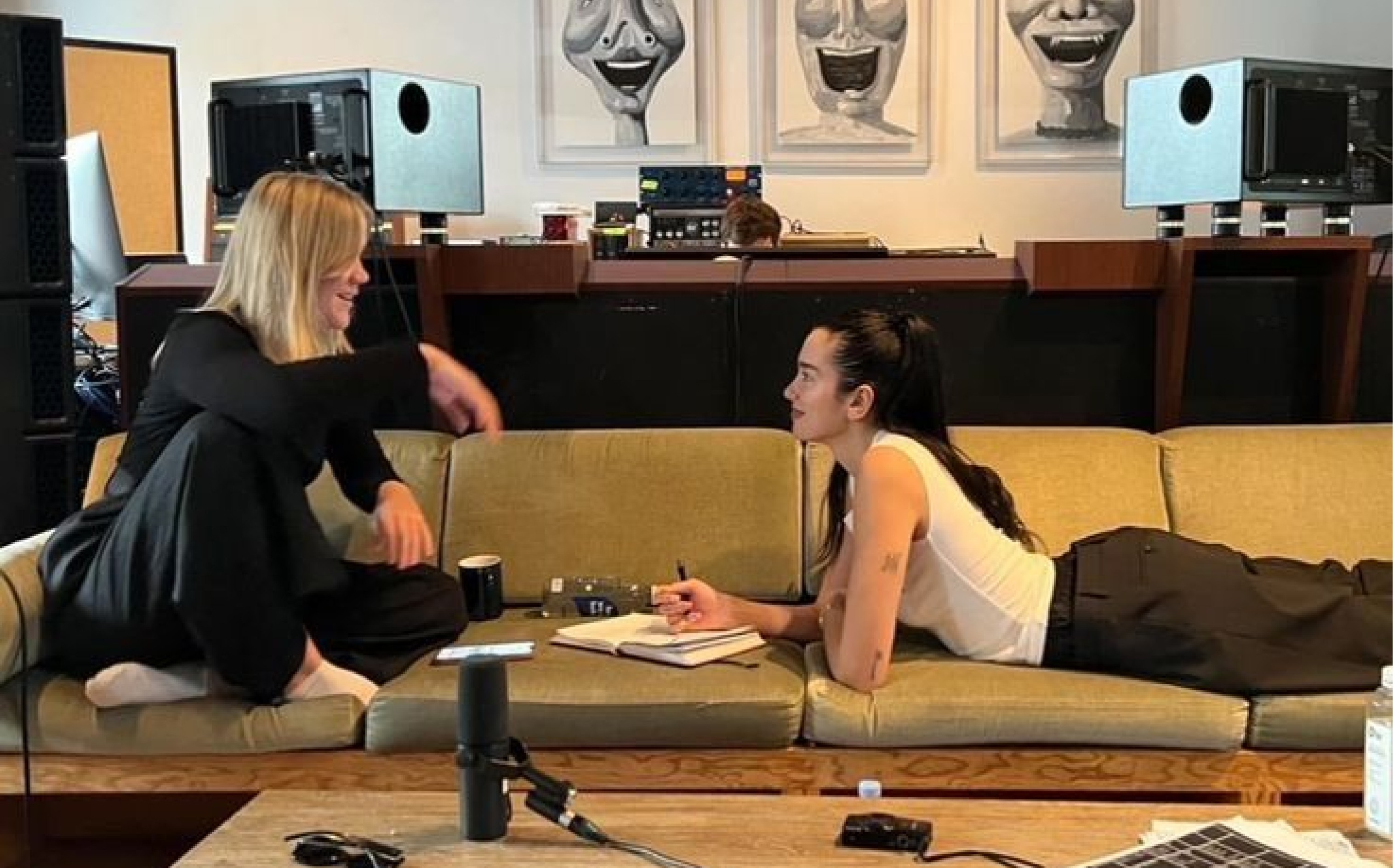 Two friends side by side on a sofa, one updating a calendar in her notepad while the other is taking a break to unwind.