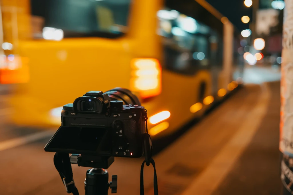 A camera on a tripod shooting a yellow bus driving passed at night