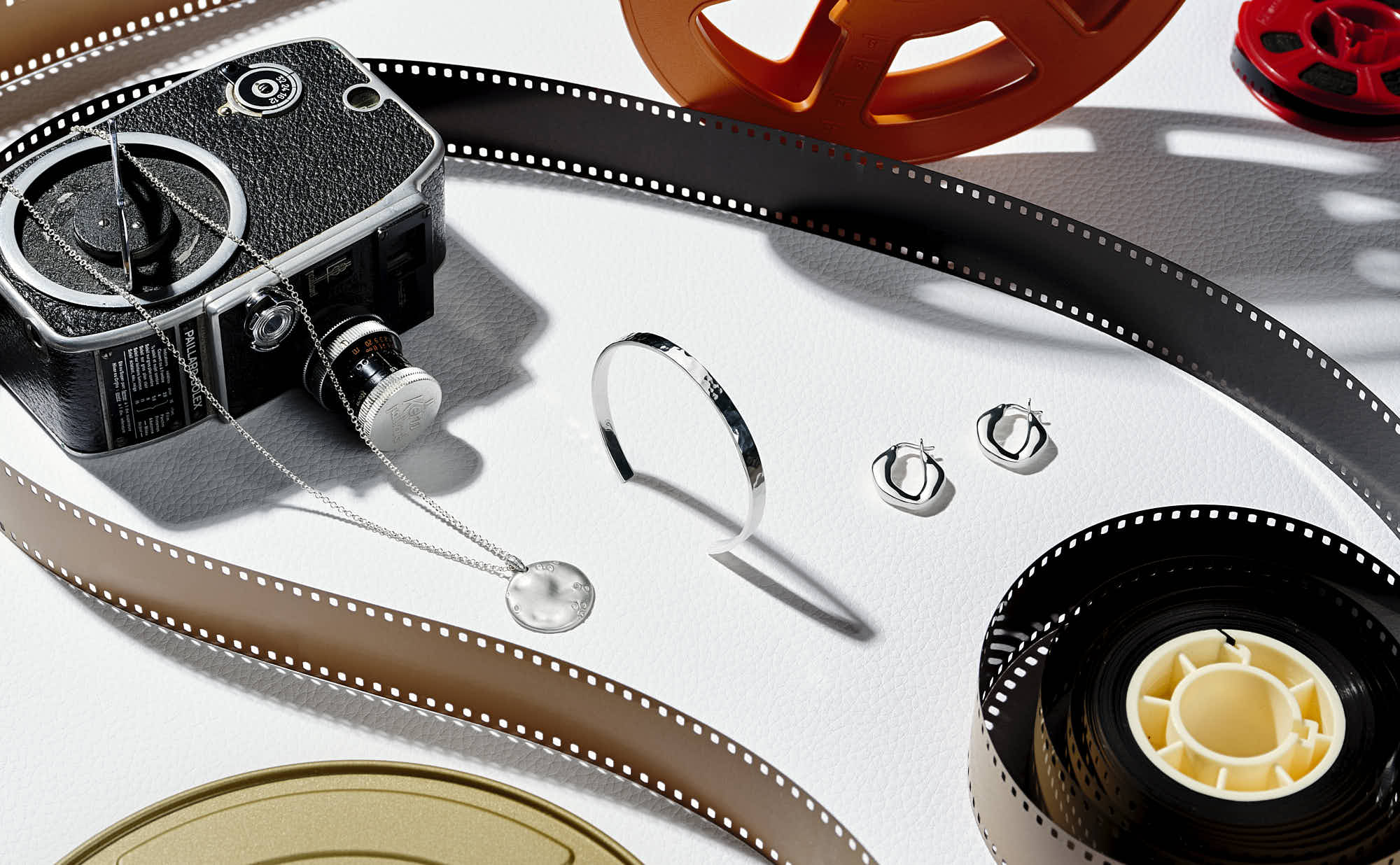 Vintage camera with film reels and silver jewelry on white background.