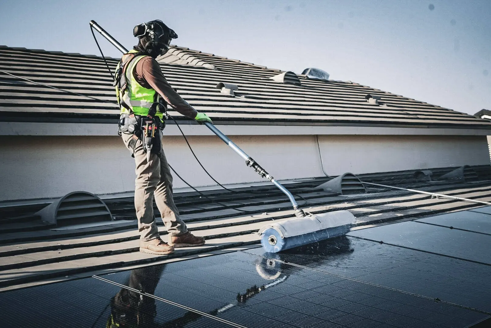 Technician in hi-vis cleaning tile-roof solar panels with a pole brush | Premier Solar Service, serving Tracy, CA