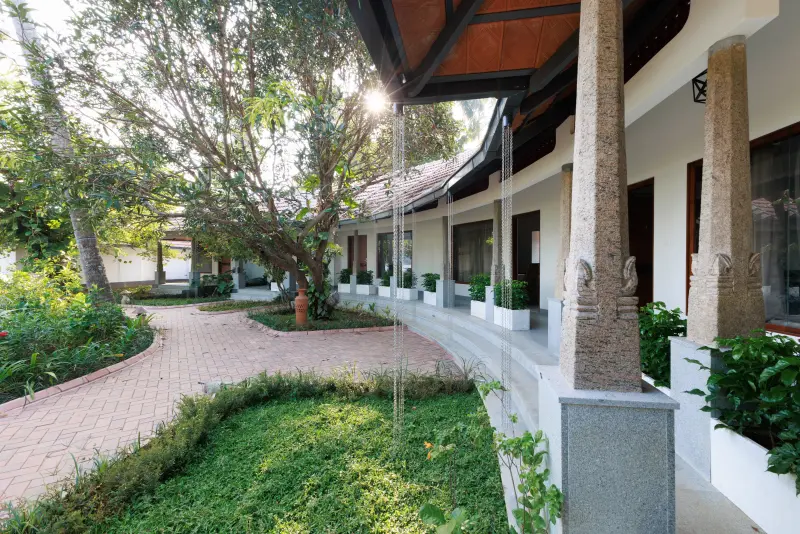 Shared courtyard at Vedic Village Kodungallur Premier Rooms with carved stone pillars, terracotta tiled roof, brick pathway and manicured garden lawn