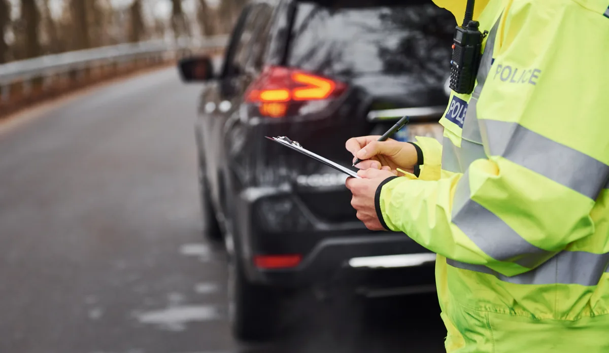 Traffic officer in a high-visibility jacket writing notes on a clipboard beside a stopped car