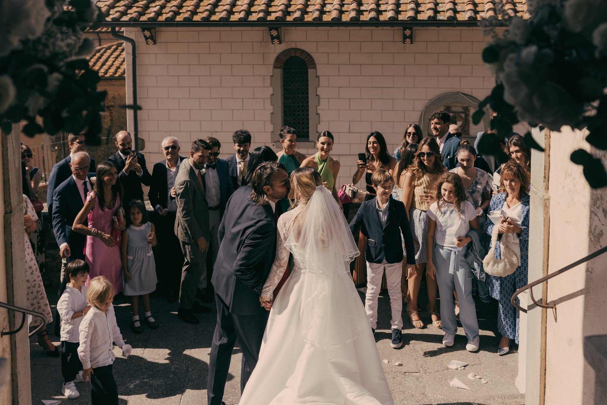 Uscita dalla chiesa a Bolgheri, sposi circondati dagli ospiti sotto il sole di settembre, reportage di matrimonio in Toscana