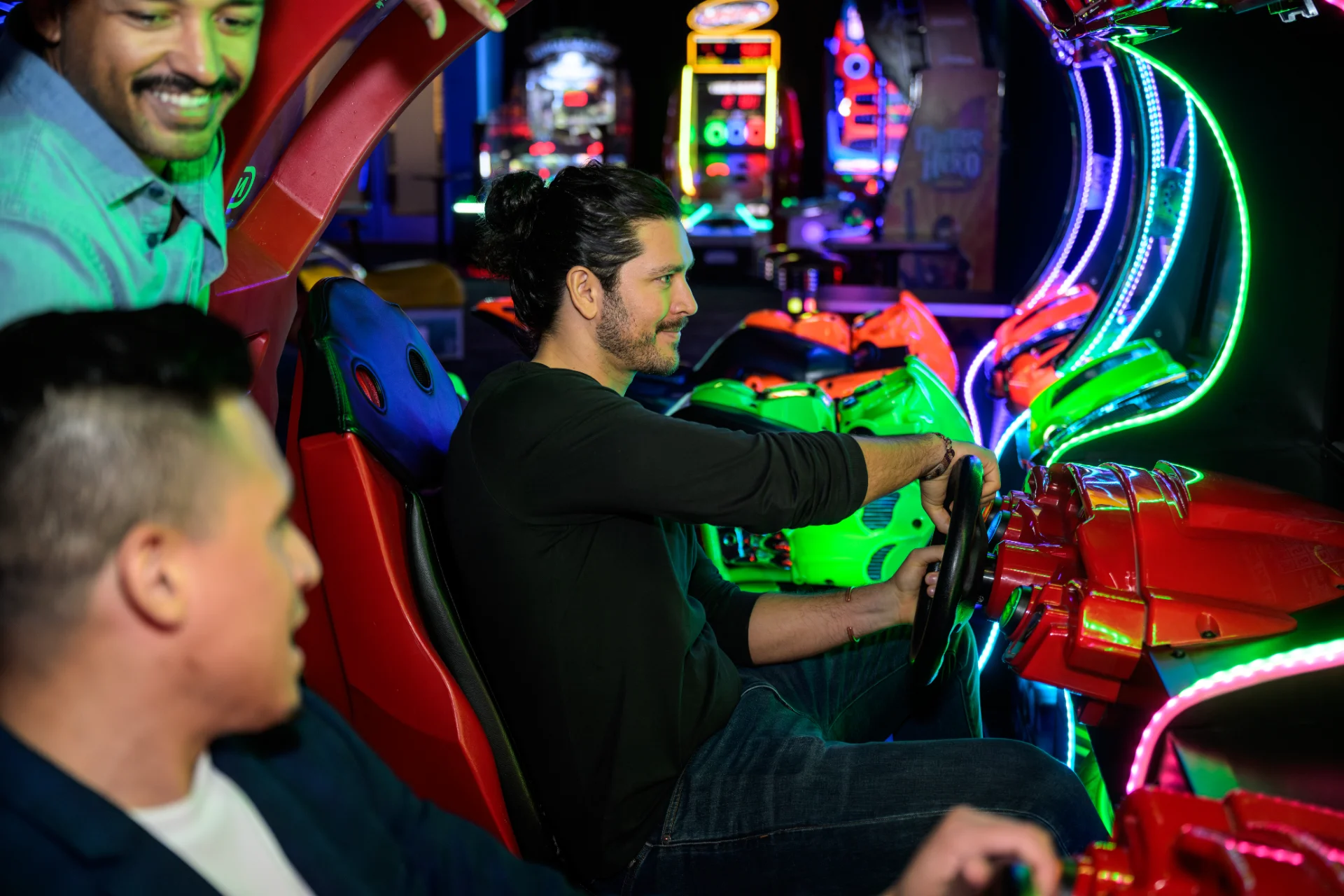 Friends racing side by side in the neon-lit driving game cabinets at Dave and Buster’s