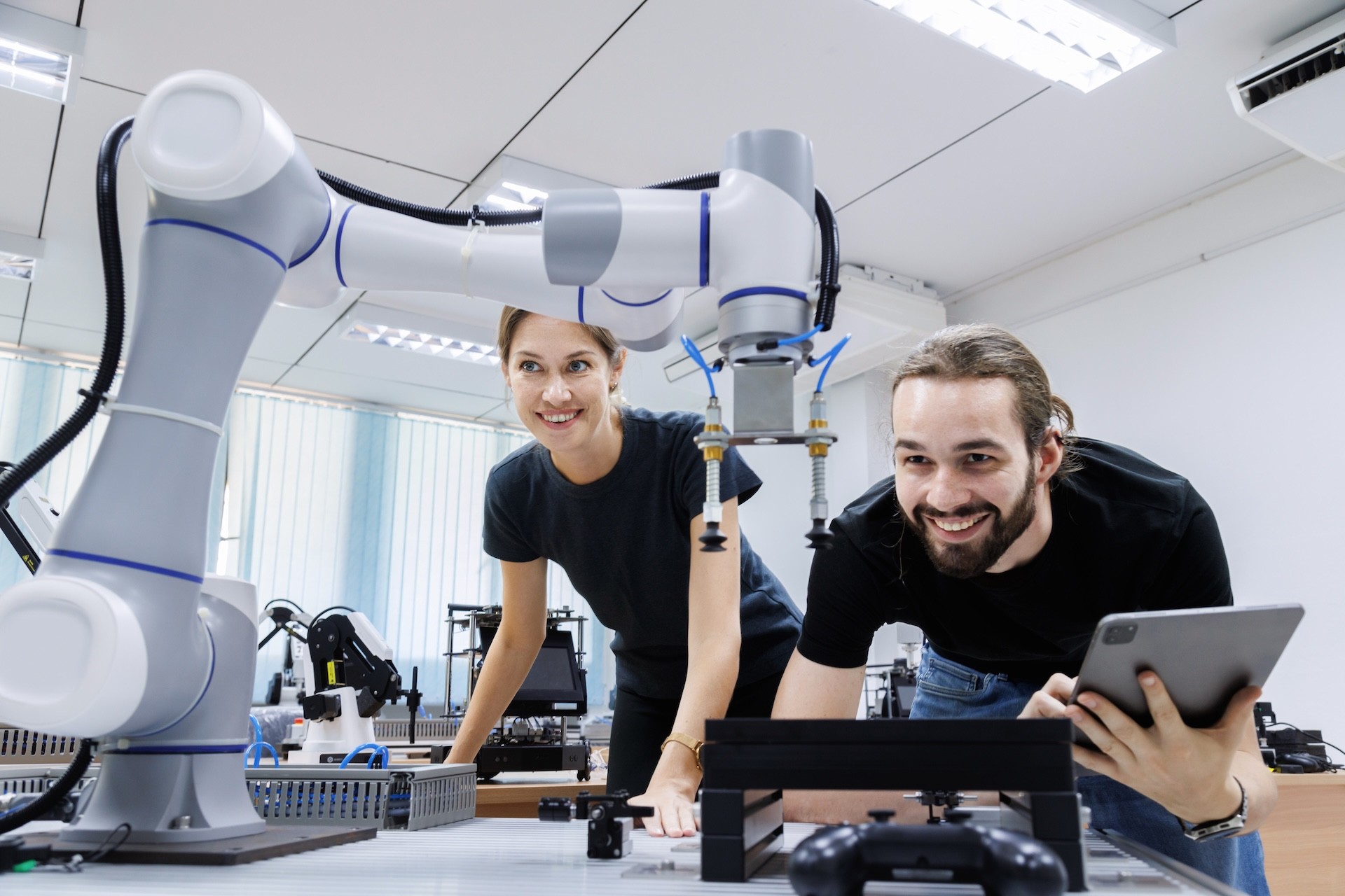 Zwei Studierende steuern einen Roboterarm in den Räumlichkeiten einer Universität.